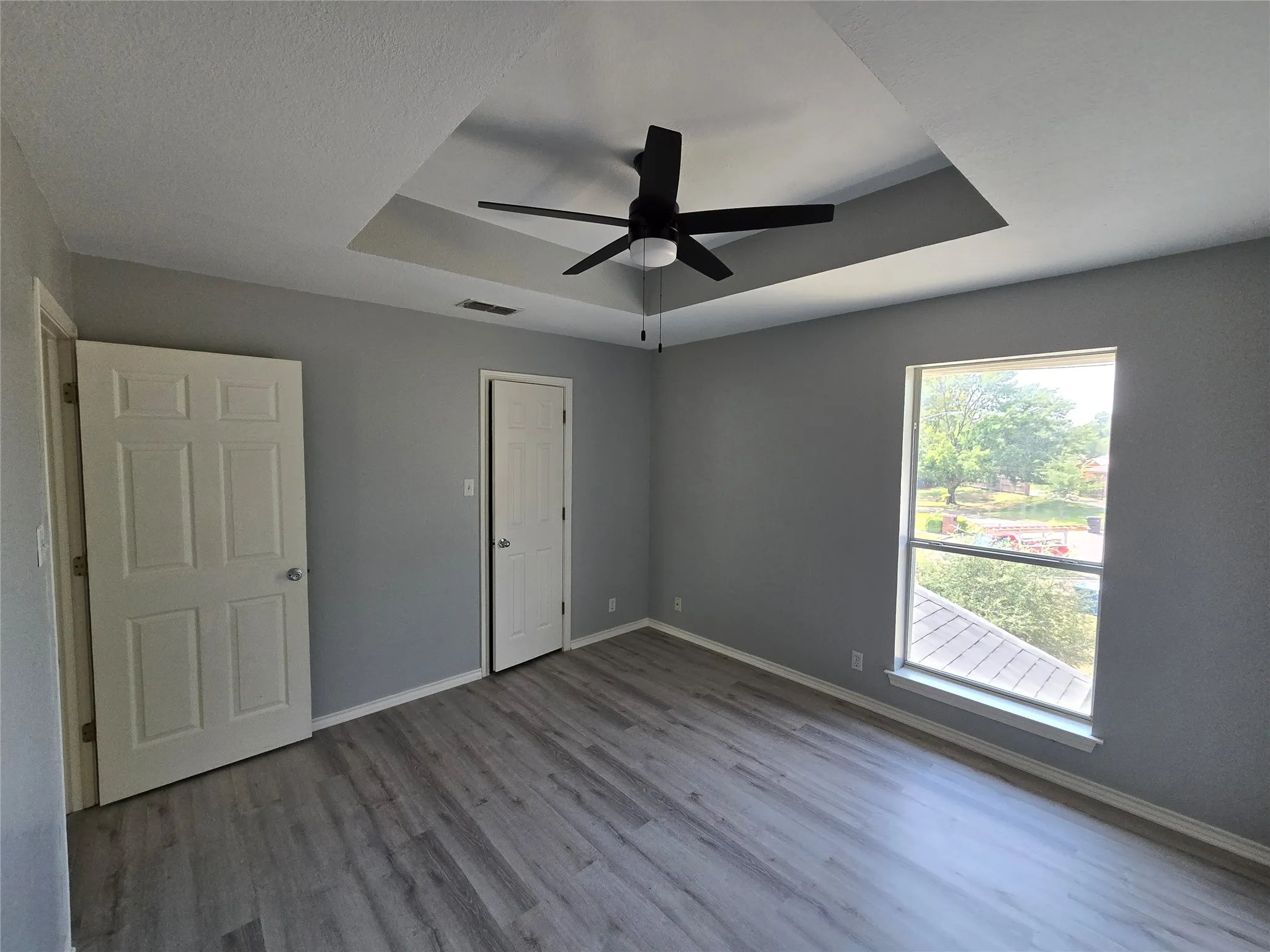 Tray ceiling with a ceiling fan, wood-finish flooring, and a large window