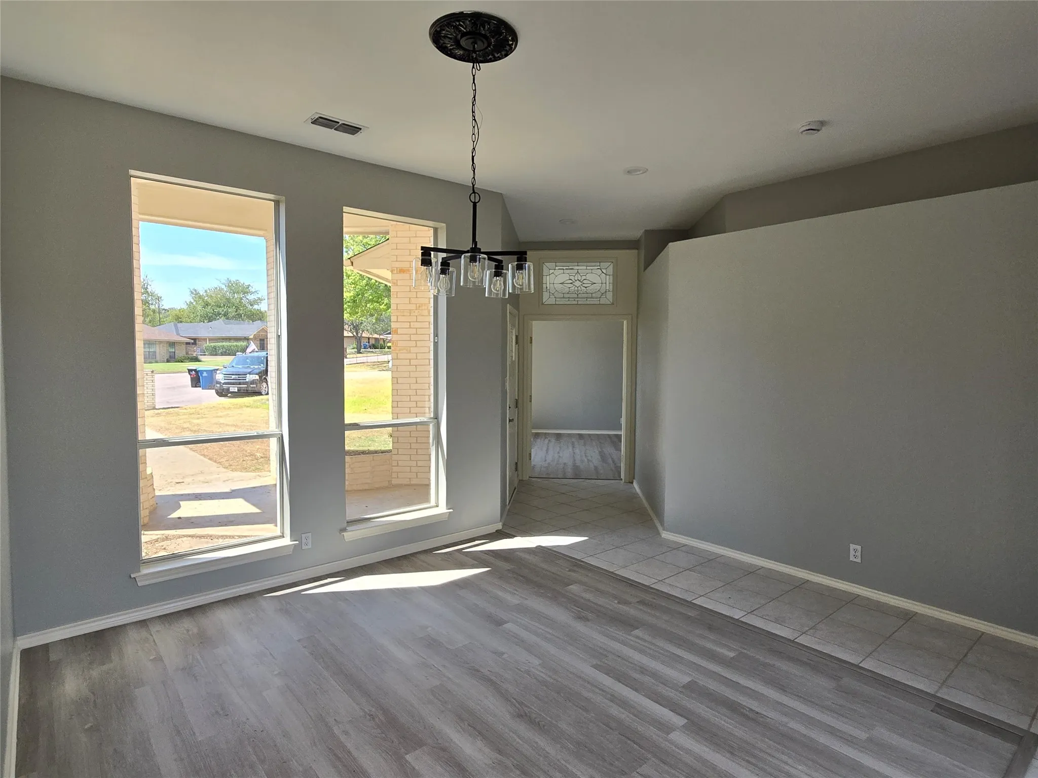 Wood-finish flooring, two large windows, an overhead chandelier, and a tiled entryway