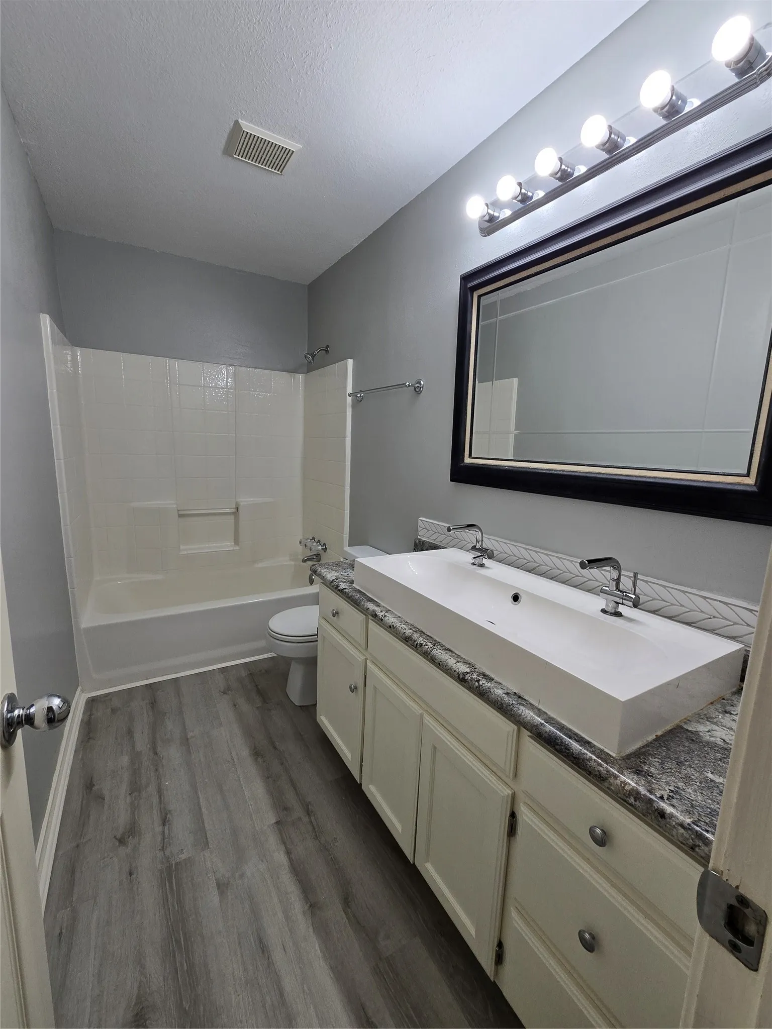 Double vanity with a rectangular basin sink, wood-finish flooring, and a shower-tub combination