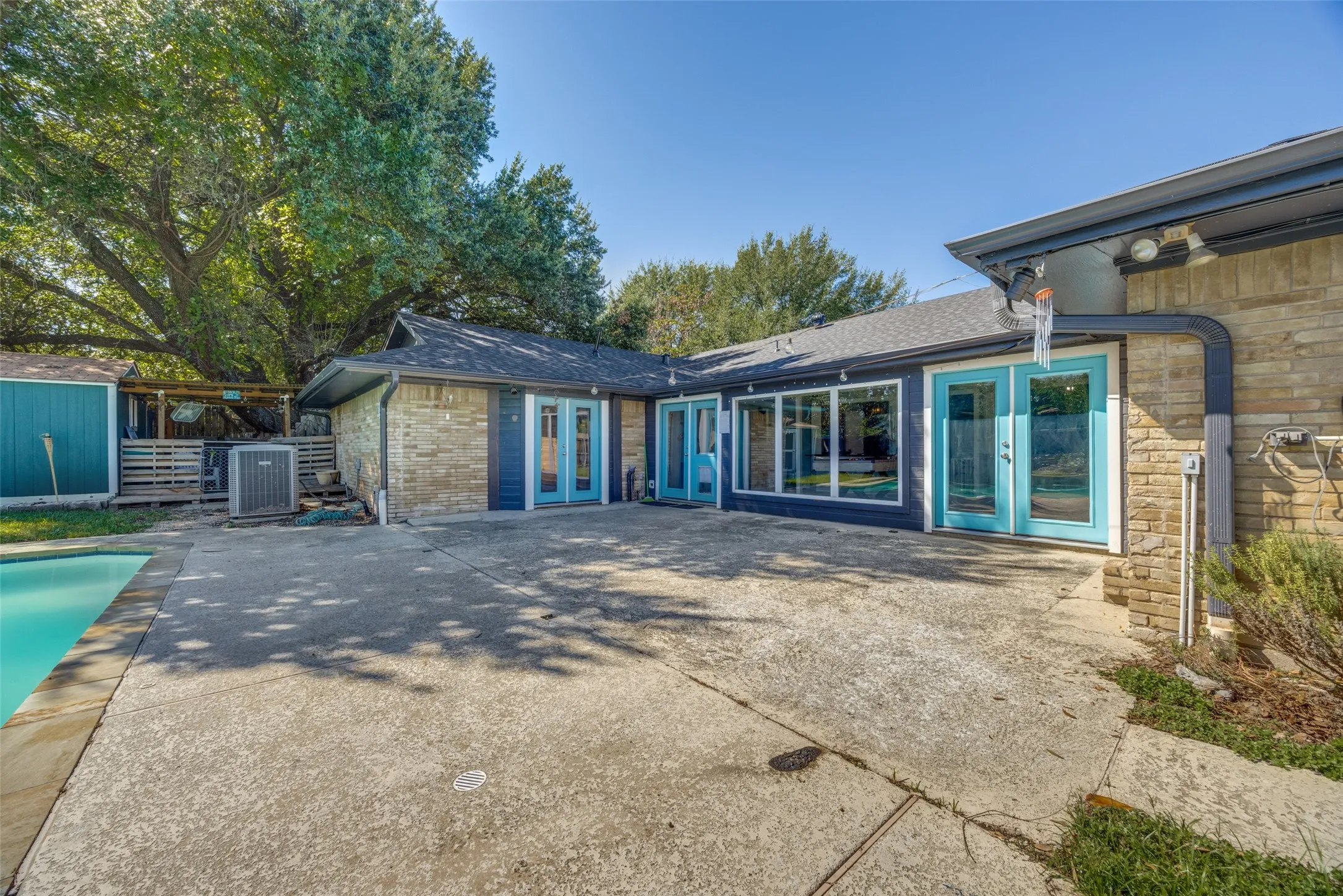 Expansive concrete patio with a swimming pool, stone exterior, and multiple glass-paneled doors