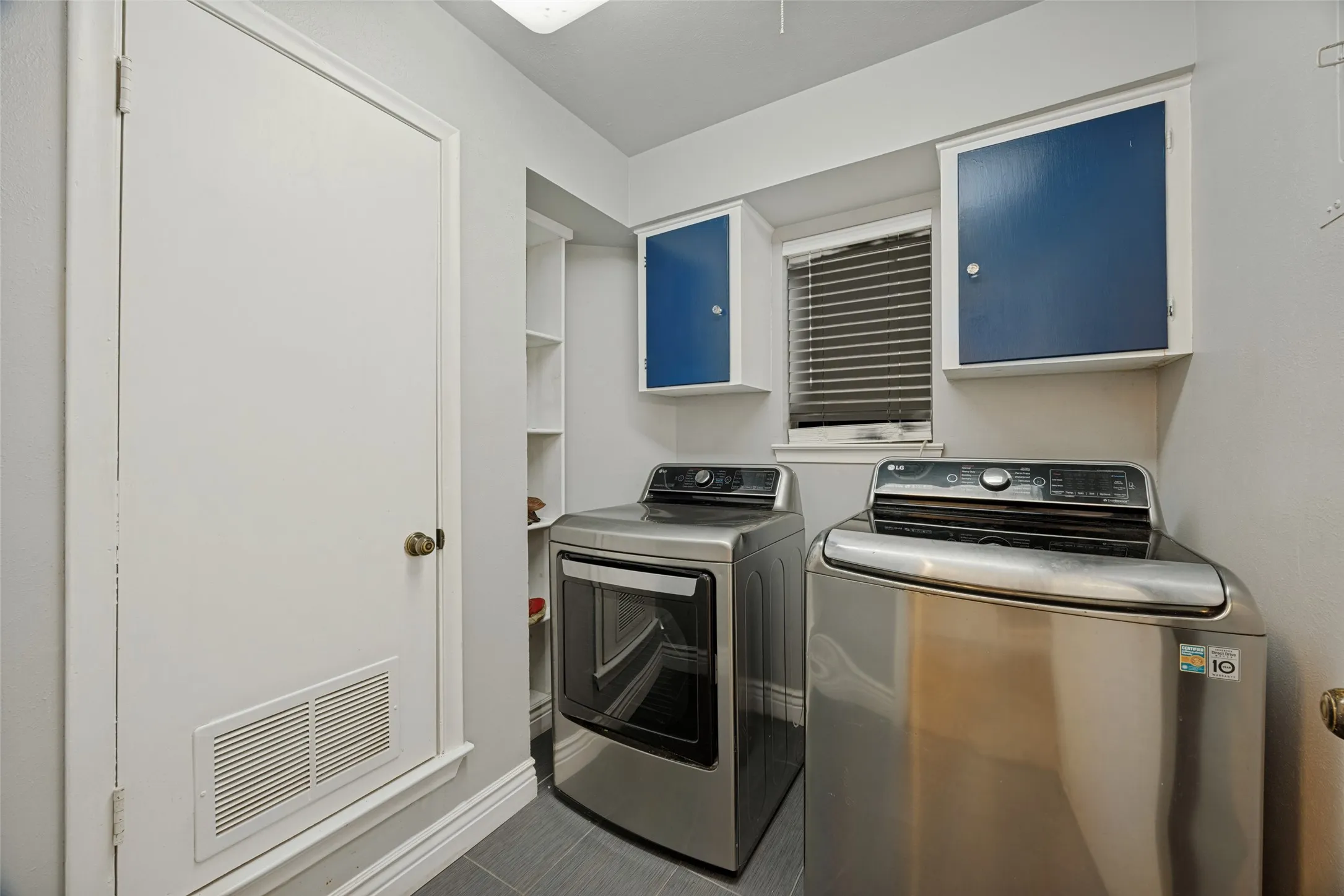 Laundry area featuring integrated shelving, upper cabinetry, and tile flooring