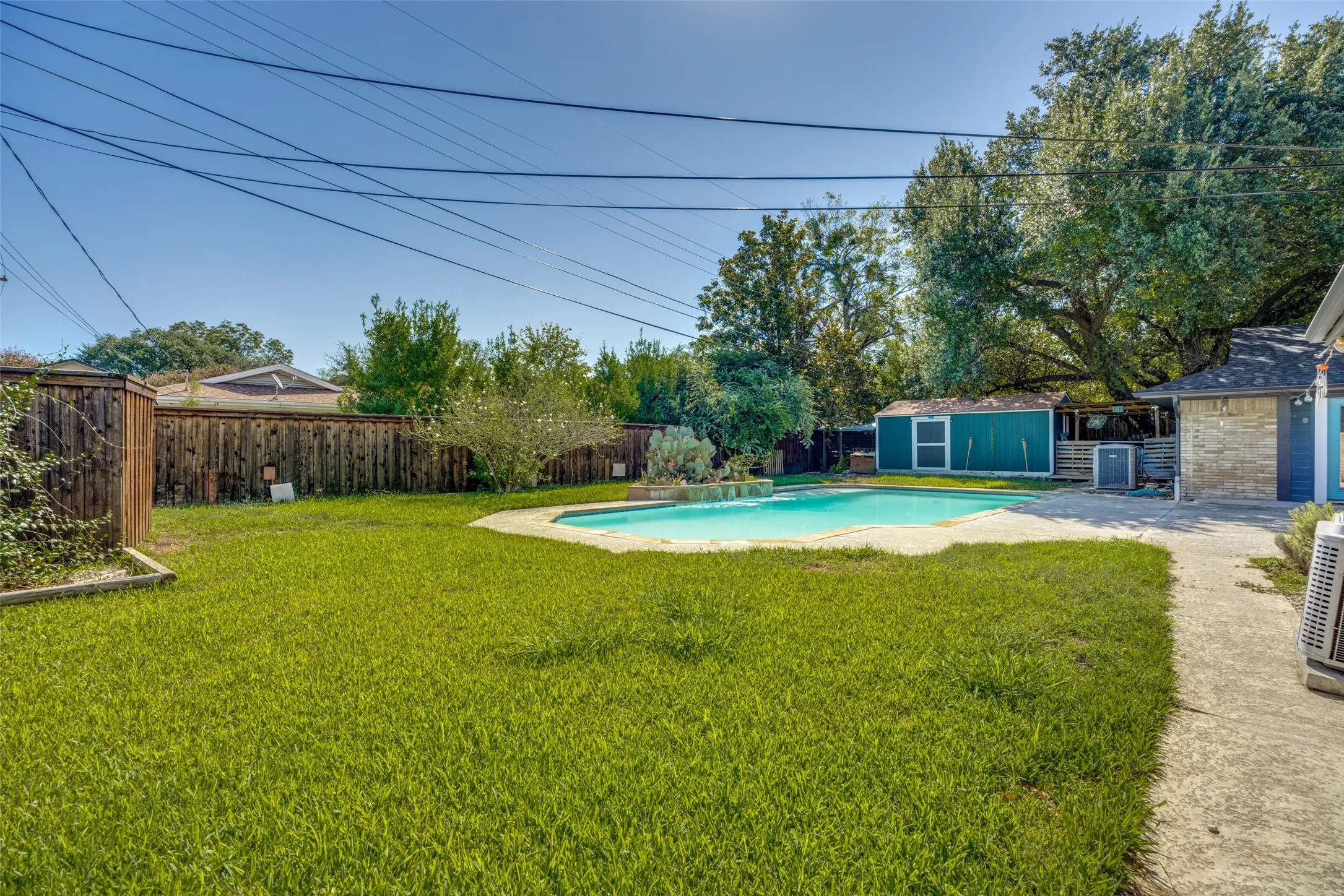 Expansive backyard featuring a swimming pool, concrete patio, a detached storage shed, and mature perimeter trees