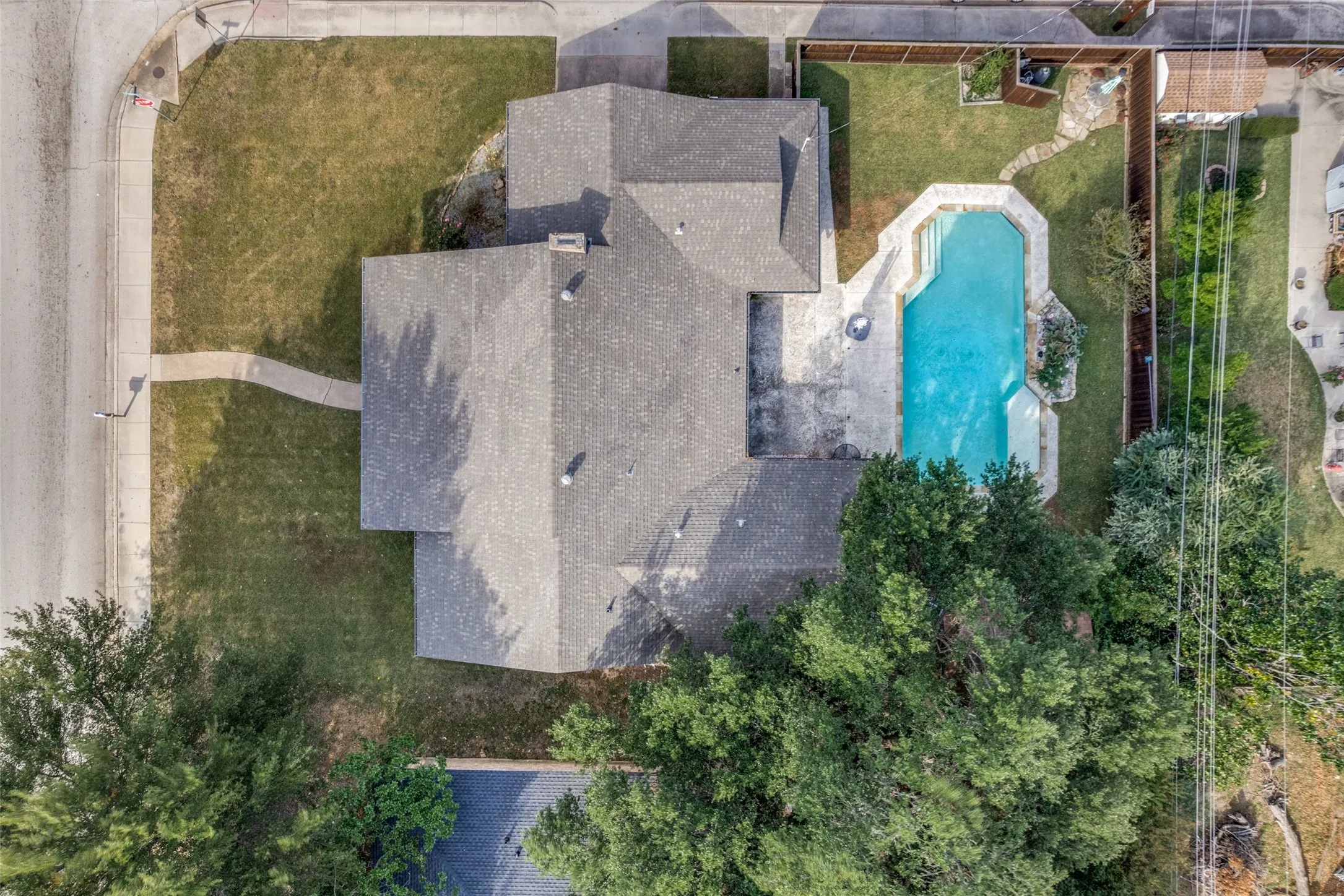 Attached pool with surrounding patio, mature trees, and fenced backyard