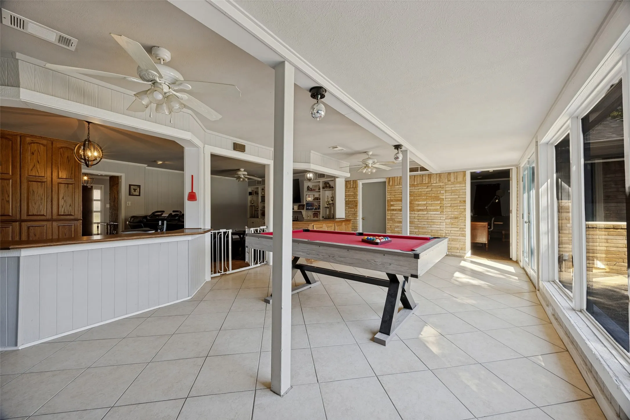 Expansive room with tiled flooring, a built-in bar with wood cabinetry, and a wall of large windows