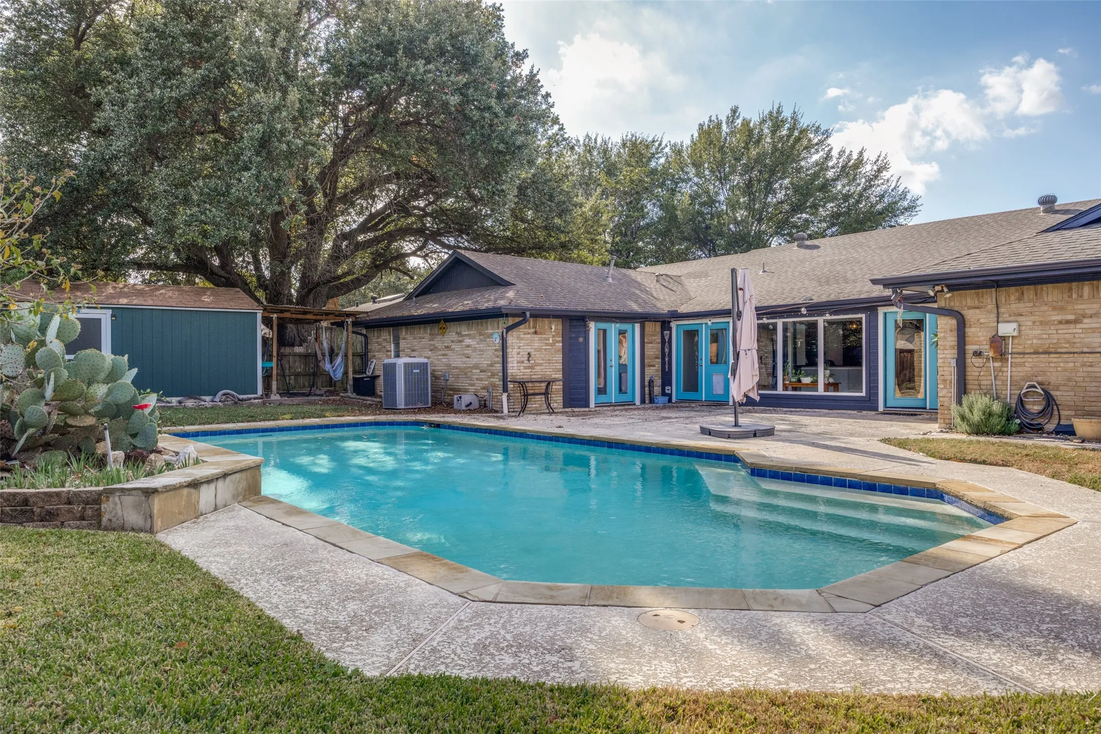 Backyard featuring a built-in swimming pool with integrated steps, a surrounding concrete patio, and a separate storage shed