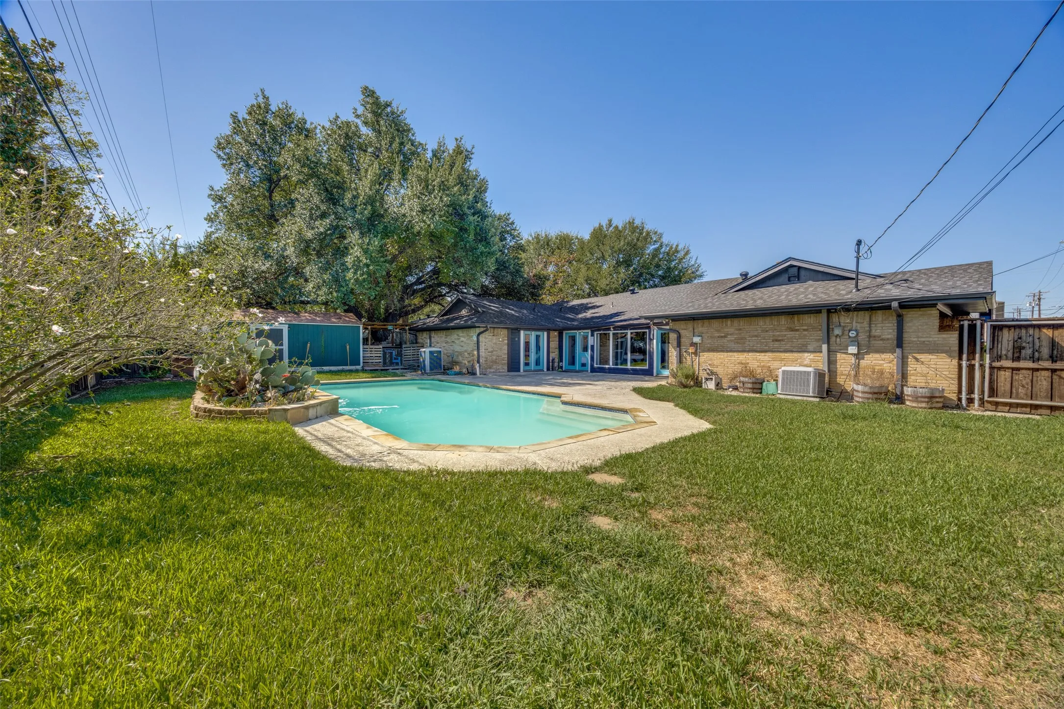 Expansive backyard featuring a swimming pool with a stone surround, a manicured lawn, and a brick-clad exterior