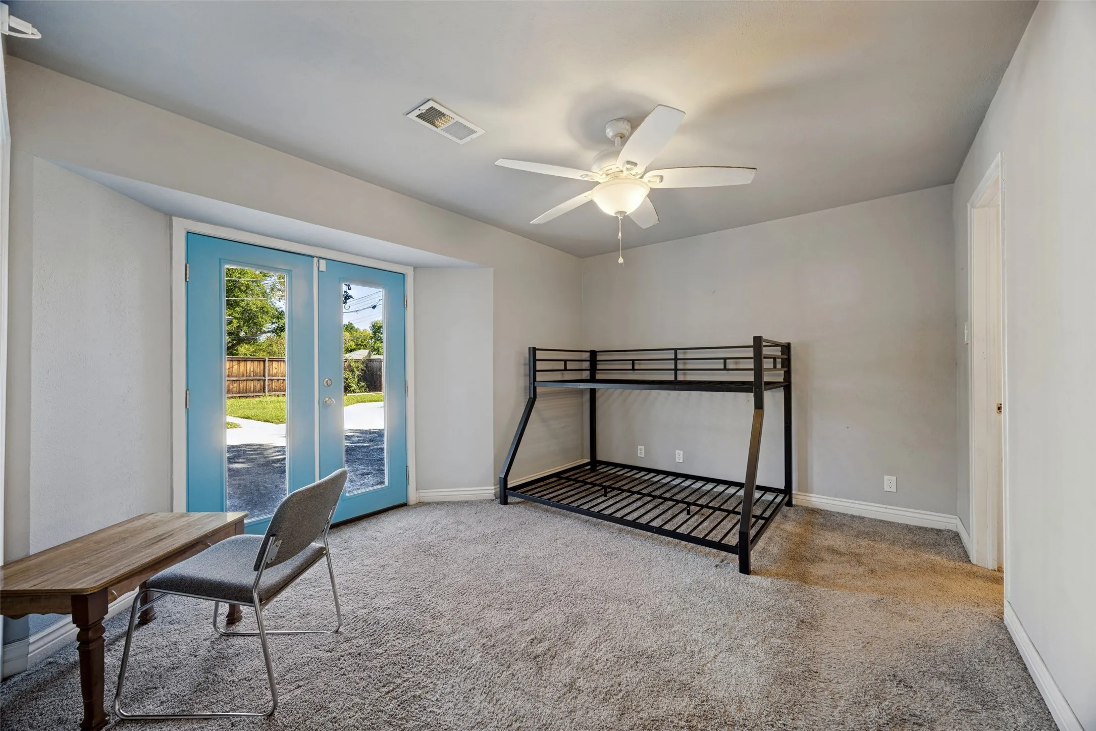 Carpeted room featuring a ceiling fan, light gray walls, and blue-framed glass panel double doors providing direct exterior access