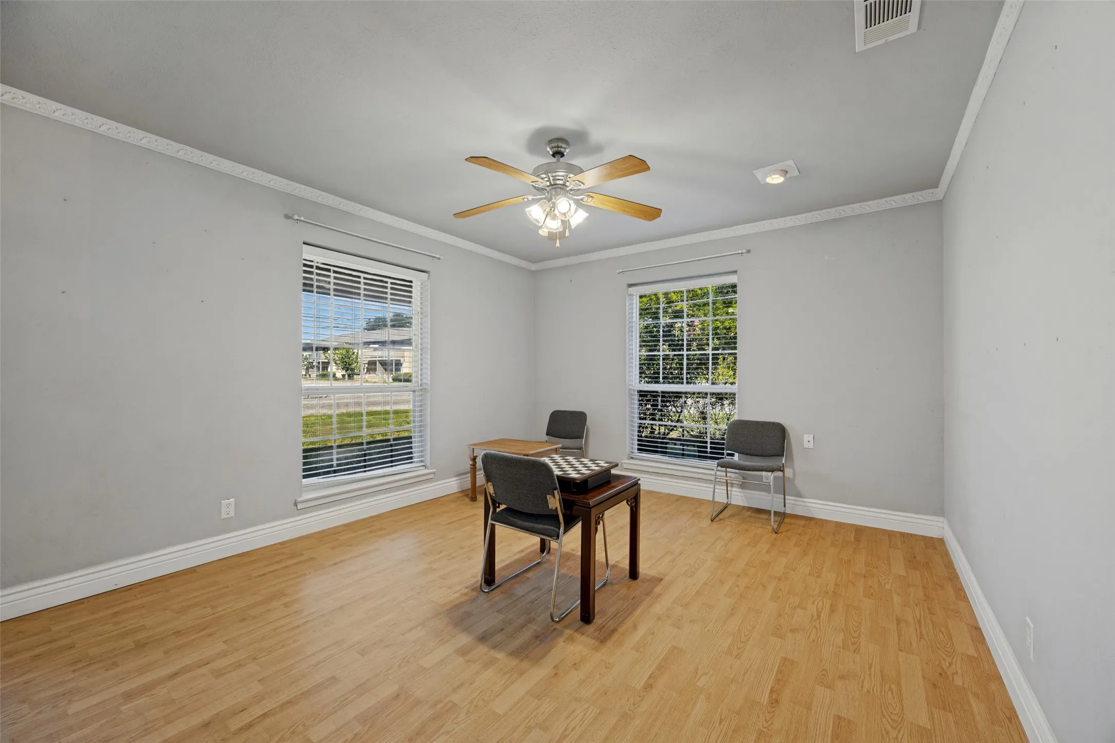 Wood-finish flooring with white baseboards, two windows with blinds, and a ceiling fan with integrated lighting