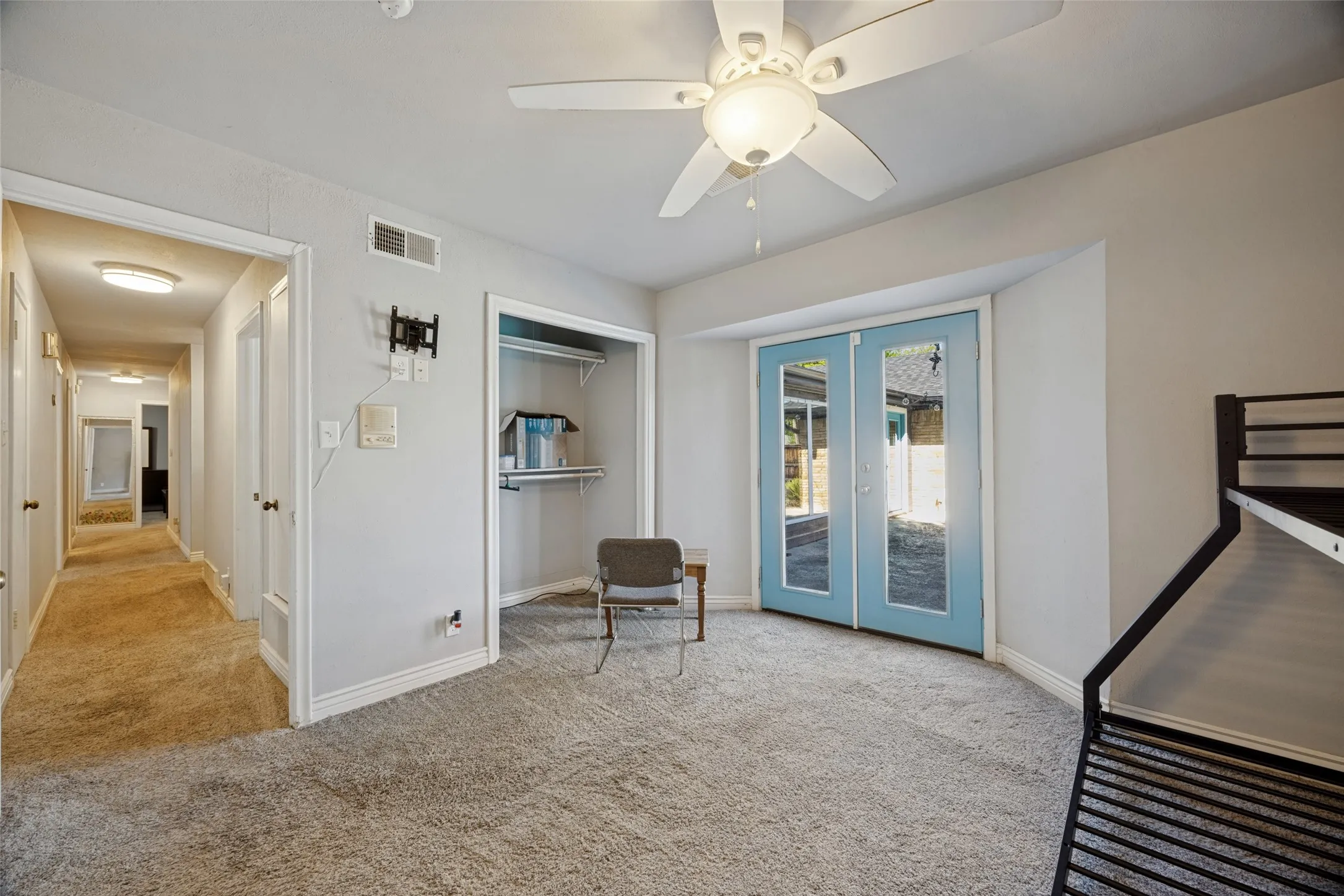 Plush carpeted flooring, a ceiling fan with integrated lighting, and light blue French doors leading to exterior