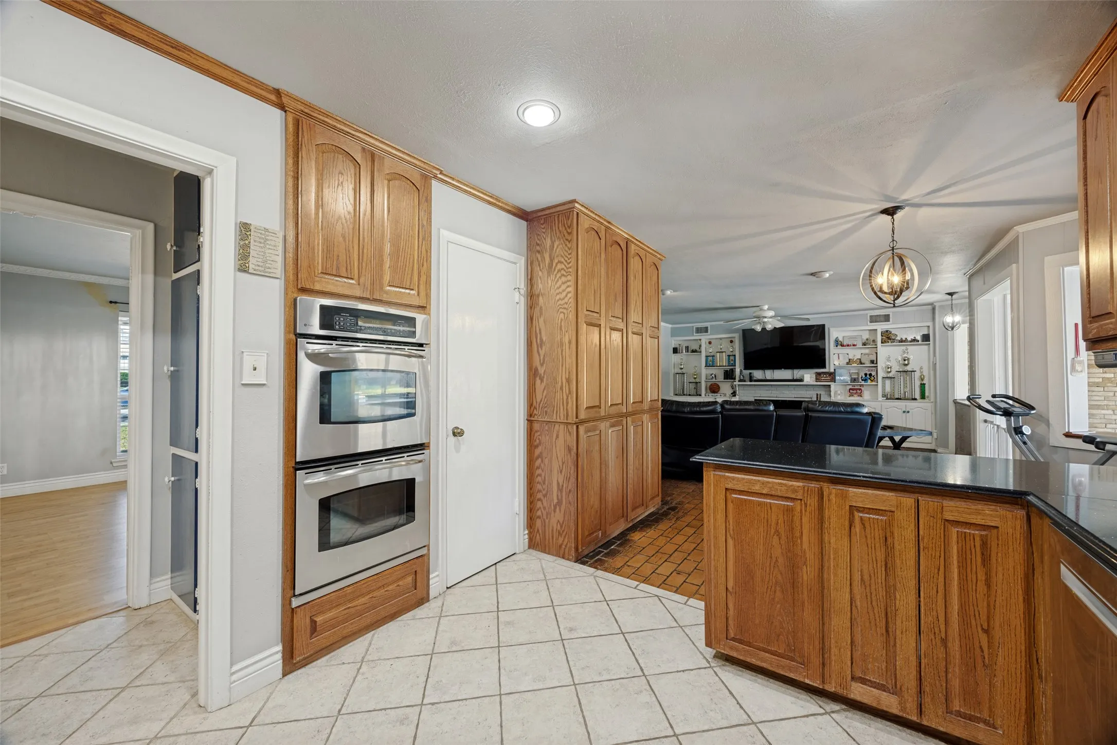 Kitchen featuring light-toned tile flooring, wood cabinetry, built-in stainless steel double ovens, and dark countertops