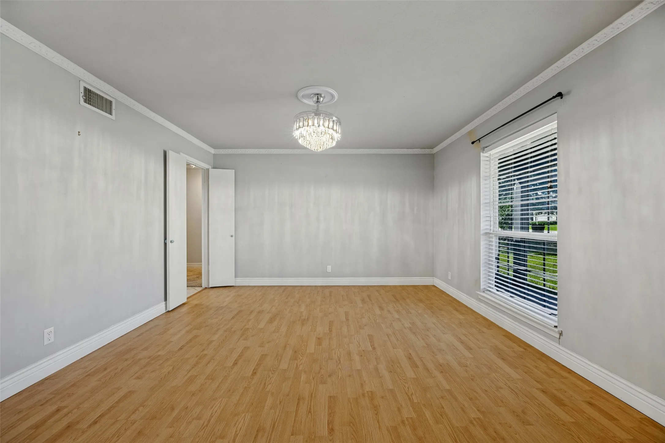 Wood-finish flooring, crown molding, double-door entry, decorative ceiling fixture, and a large window with blinds