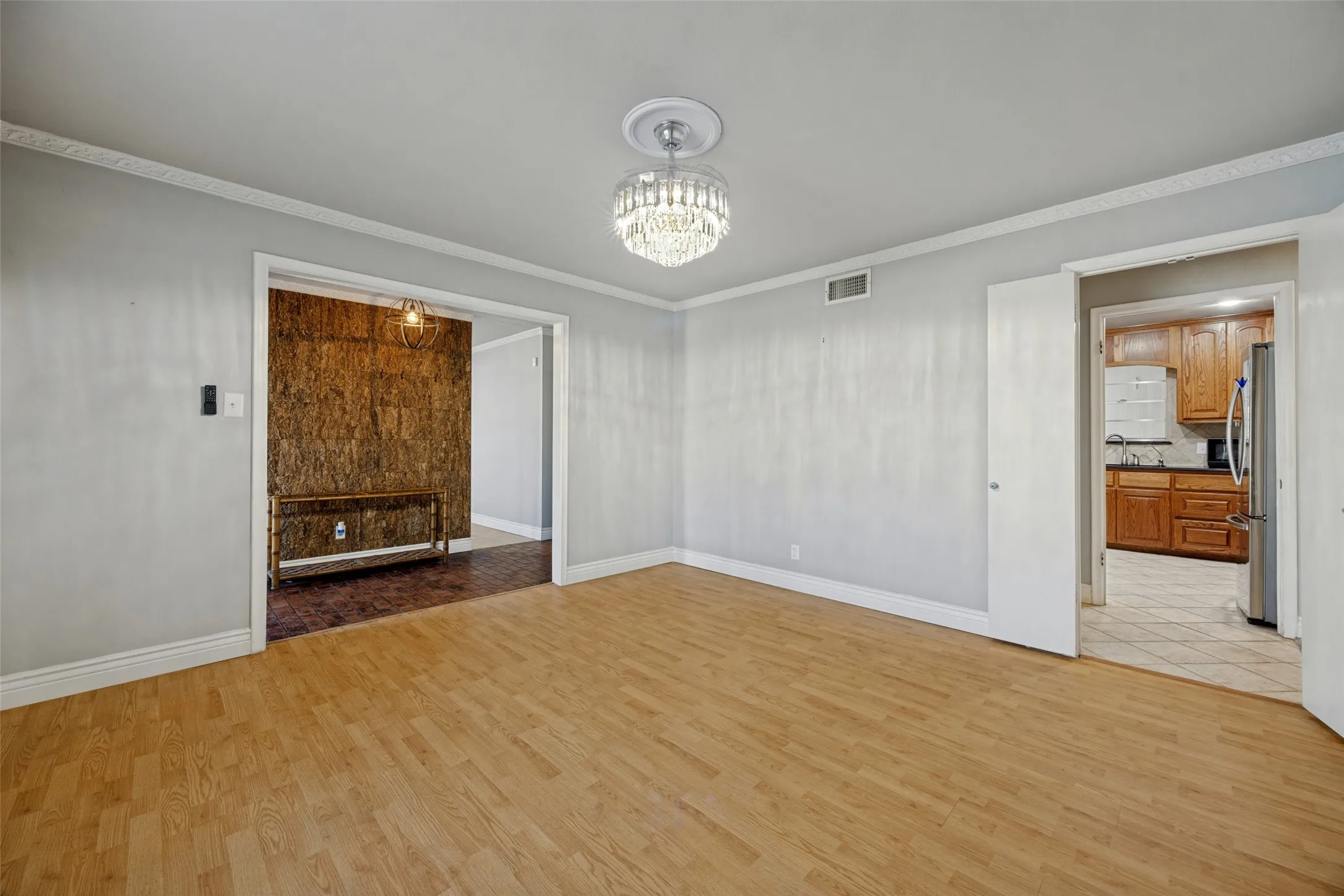 Light wood-finish flooring, crown molding, and a crystal chandelier