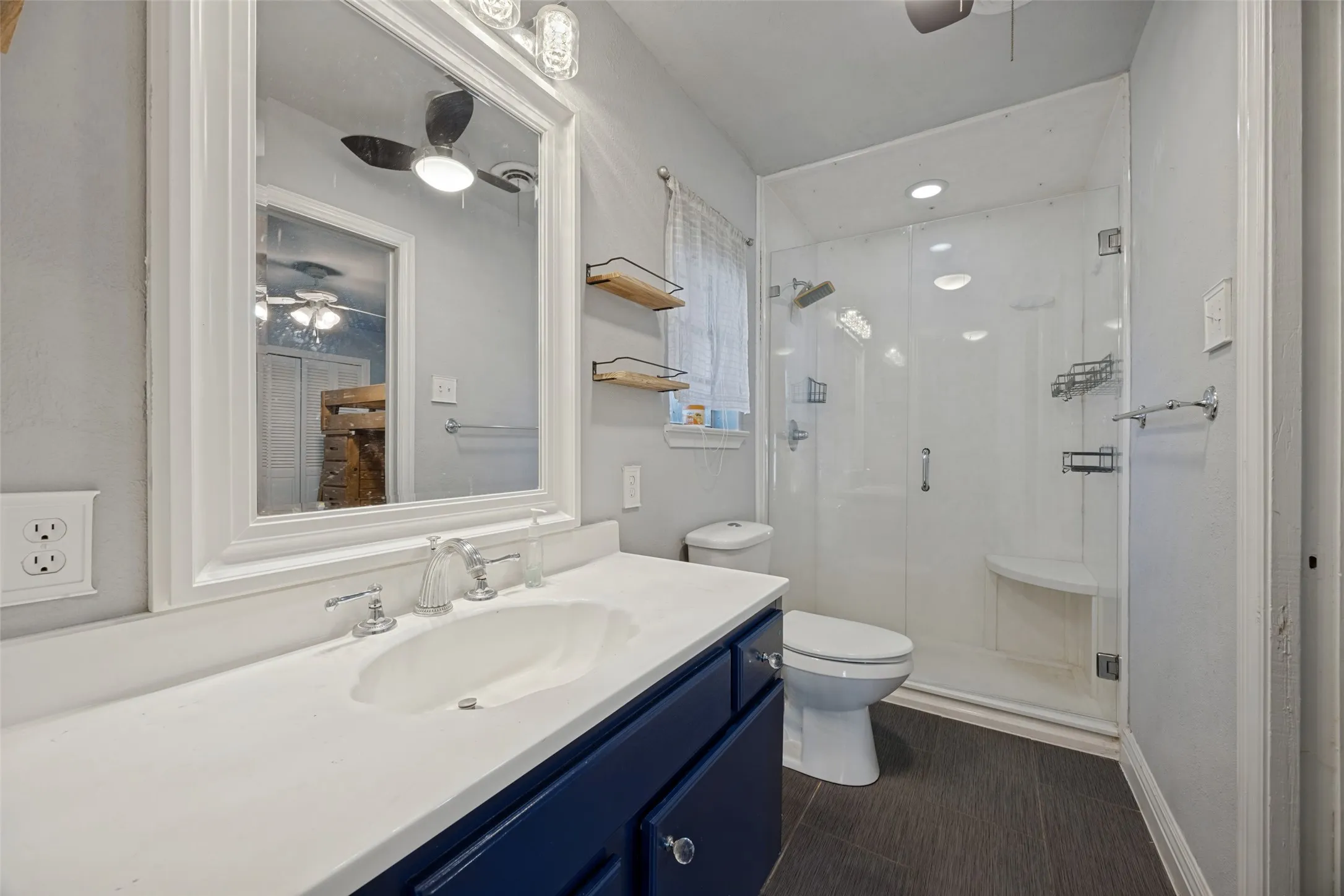Built-in vanity with a white countertop and navy cabinetry, framed mirror, and a glass-enclosed shower with a built-in bench
