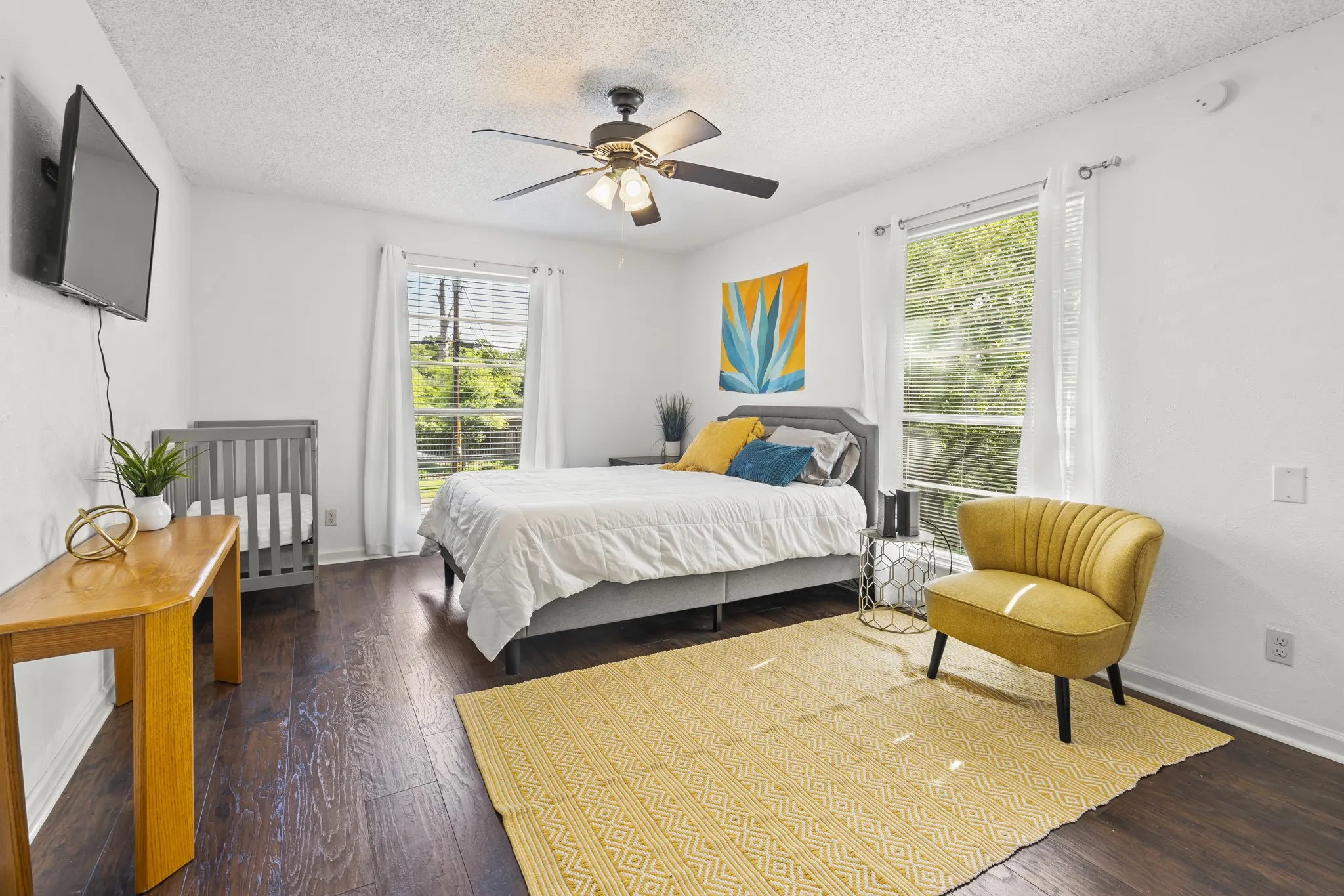 Wood-finish flooring, white walls, two large windows, and a ceiling fan with integrated lighting