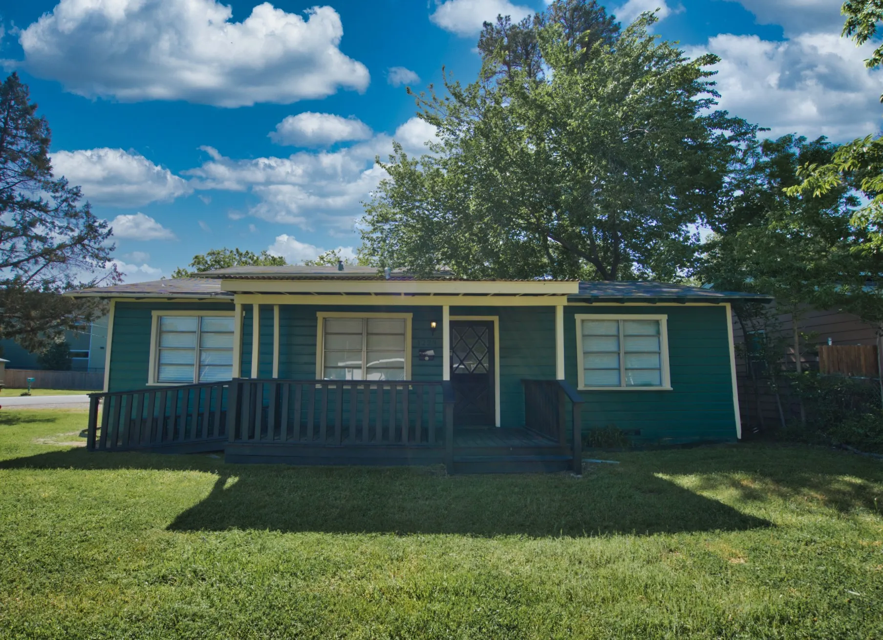 Green exterior siding with white trim, front porch with dark railing, and a ramp entrance