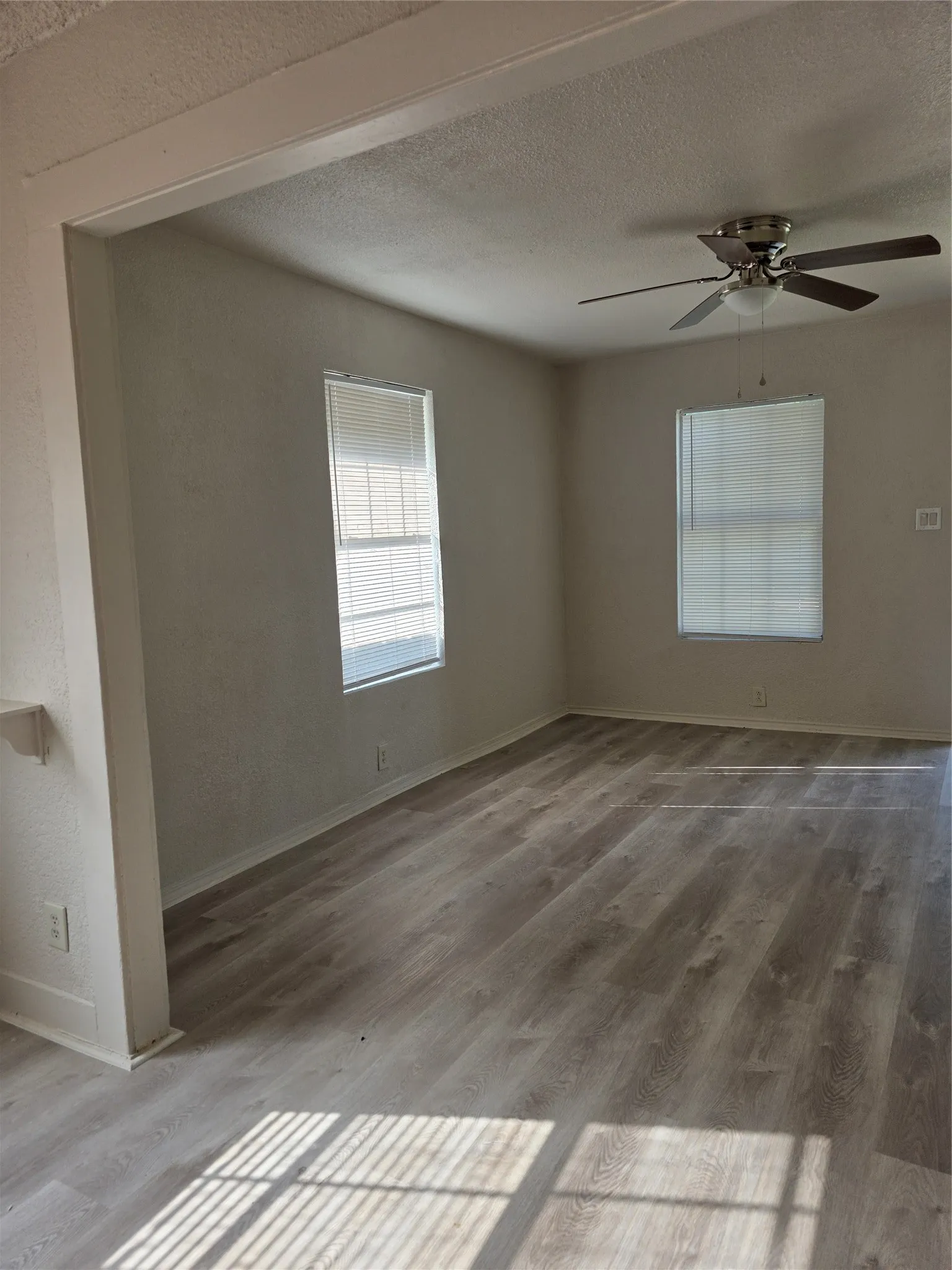 Spacious room featuring wood-finish flooring, multiple windows with blinds, and a ceiling fan with integrated lighting