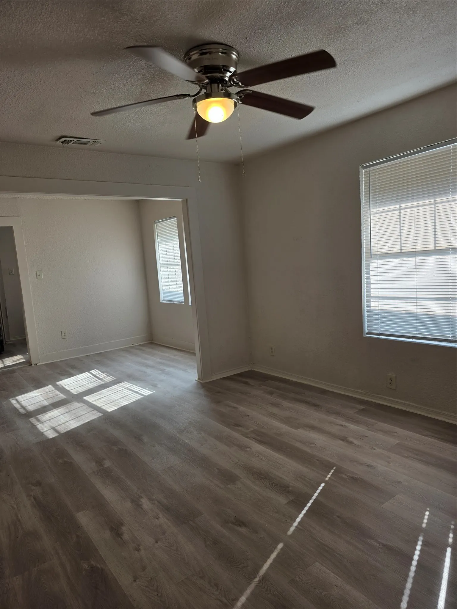 Wood-finish flooring throughout, ceiling fan with integrated lighting, and multiple windows with blinds
