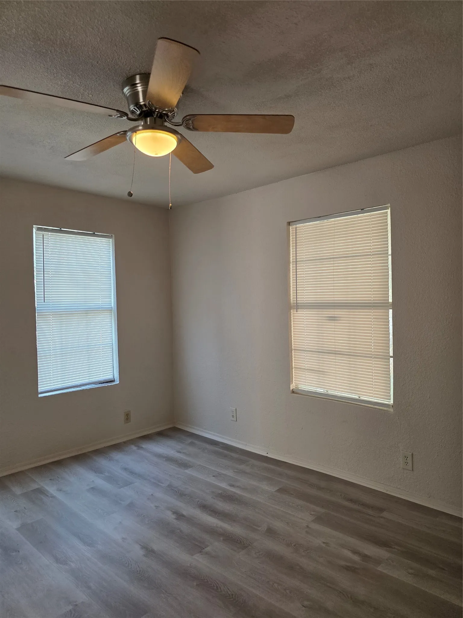 Wood-finish flooring, two windows with blinds, ceiling fan with integrated lighting, and neutral wall tones
