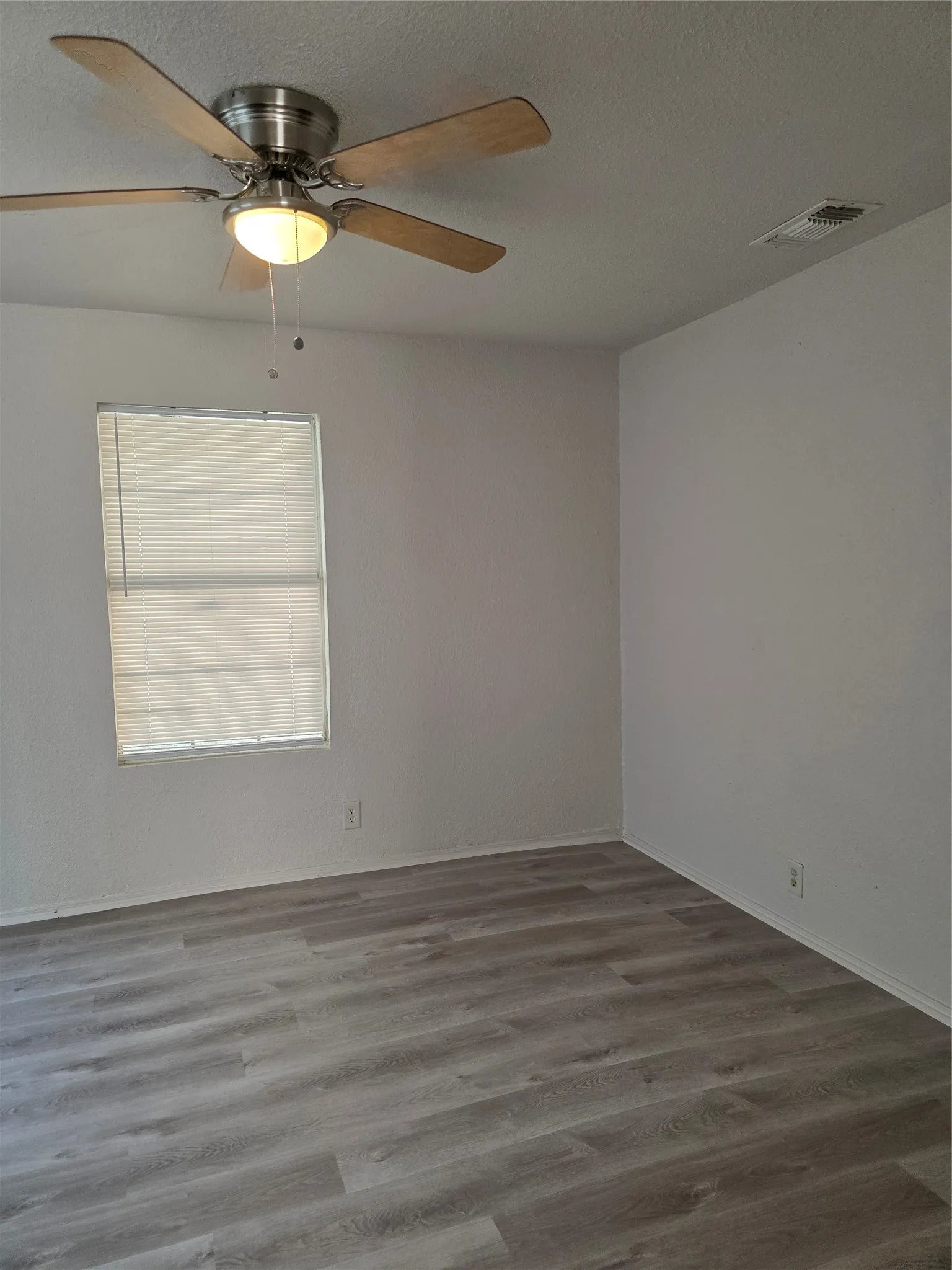 Wood-finish flooring, ceiling fan with integrated lighting, window with blinds, and painted walls