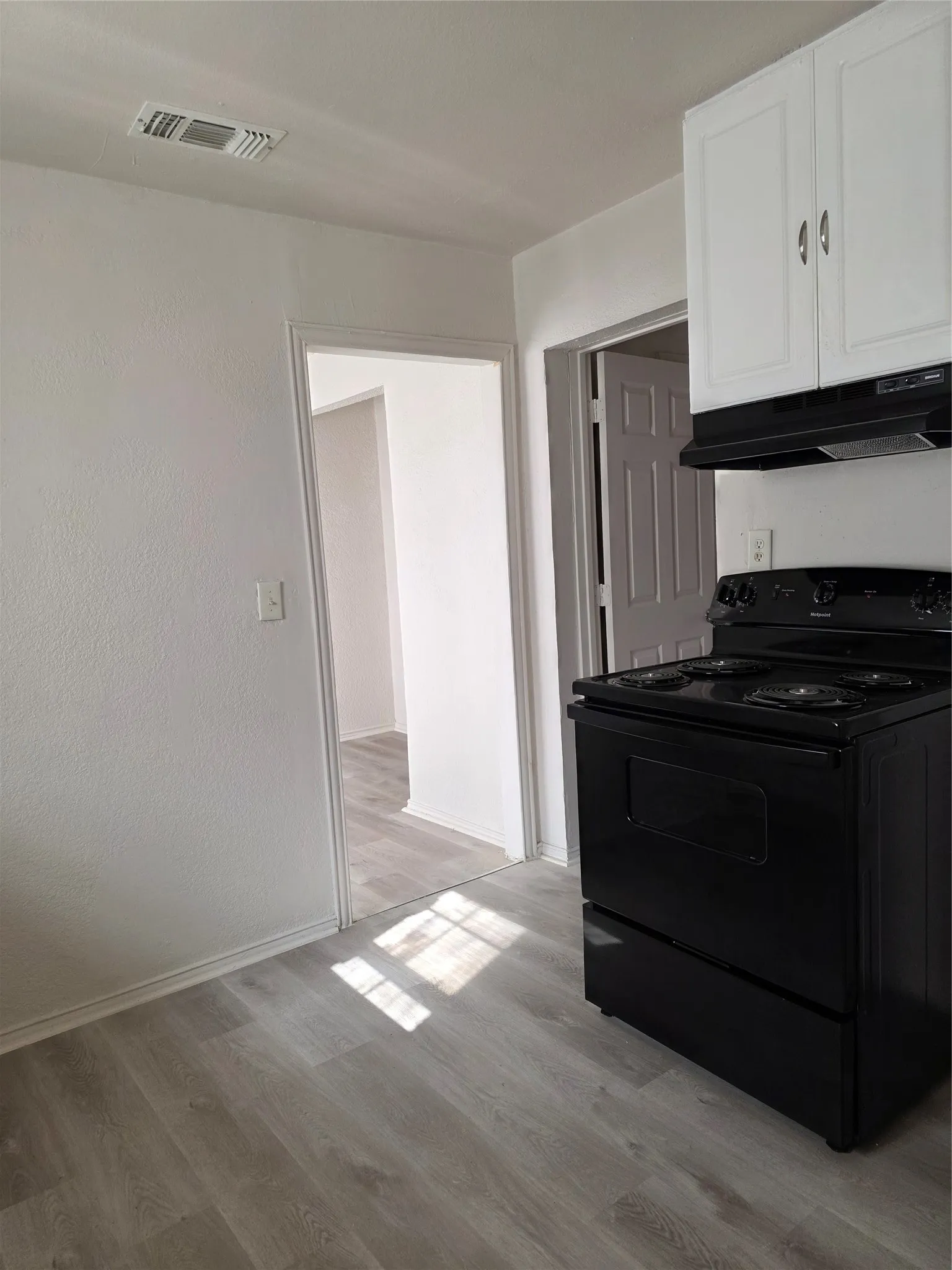 White upper cabinetry with silver hardware, integrated black range hood, and black electric range
