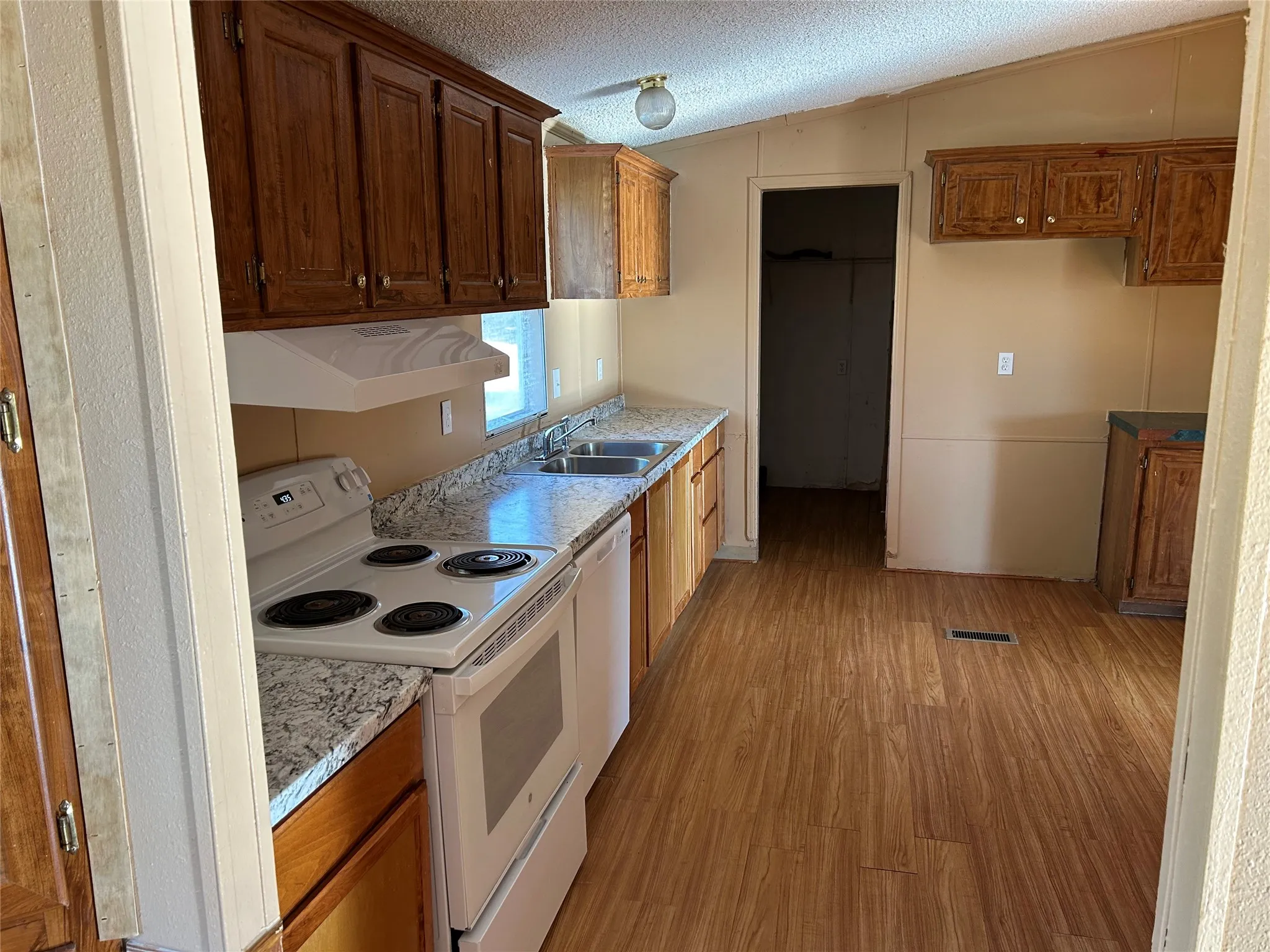 Kitchen featuring wood-finish flooring, wood cabinetry, white appliances, and a double basin sink