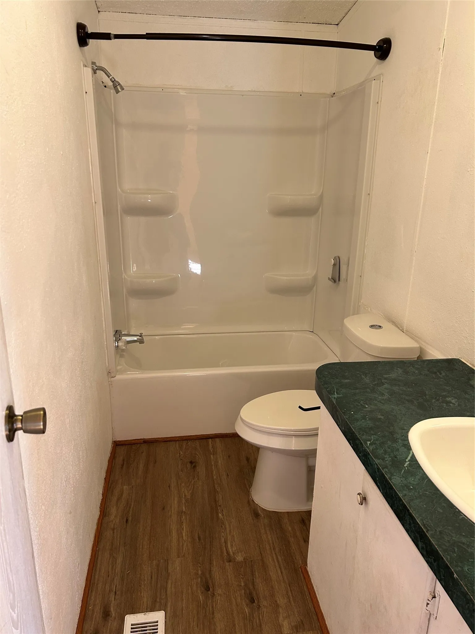 Bathroom featuring a combination bathtub/shower unit, wood-finish flooring, toilet, and vanity with an integrated sink