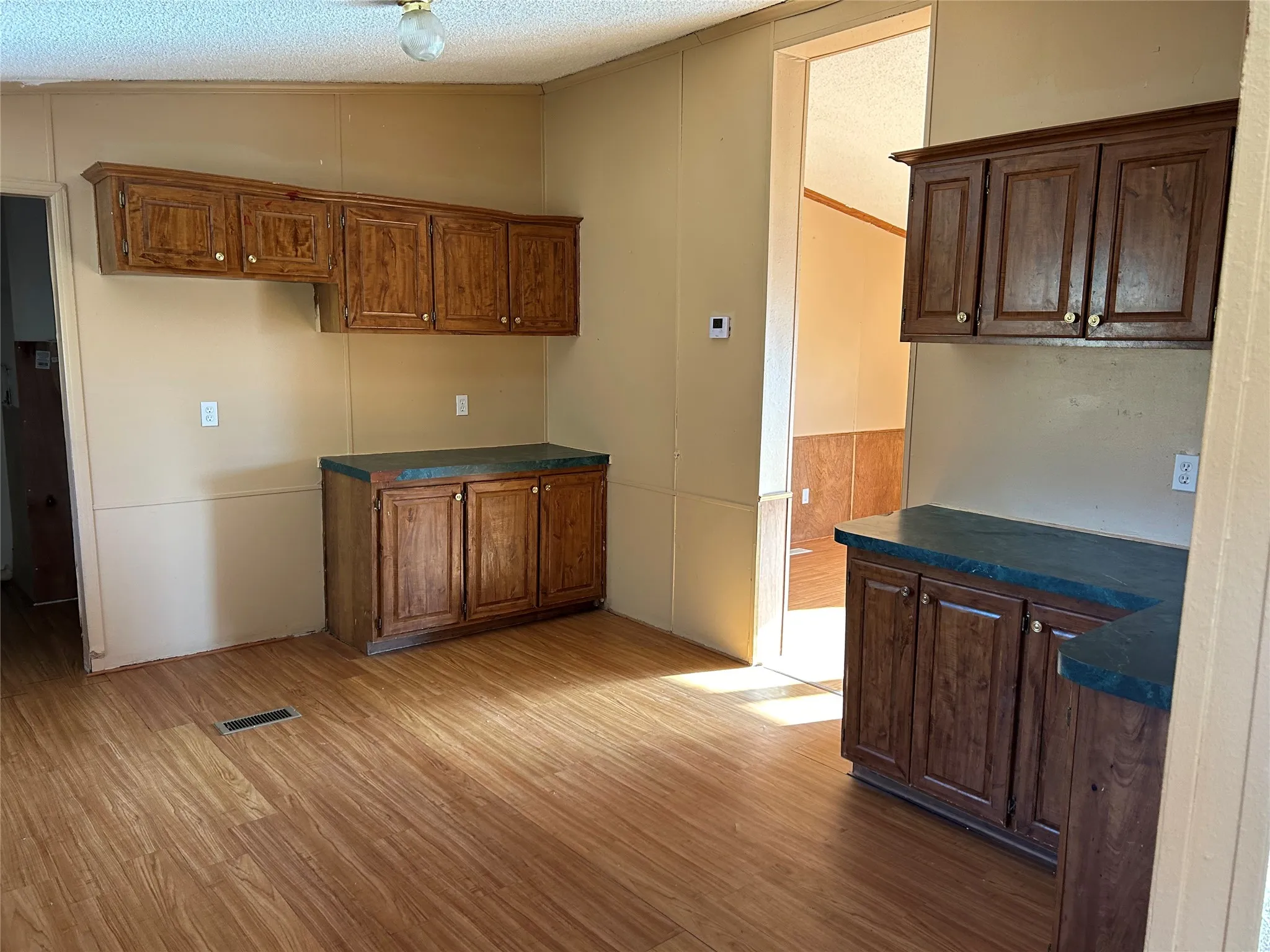 Wood-finish flooring, wood cabinetry with gold-tone hardware, and dark countertops