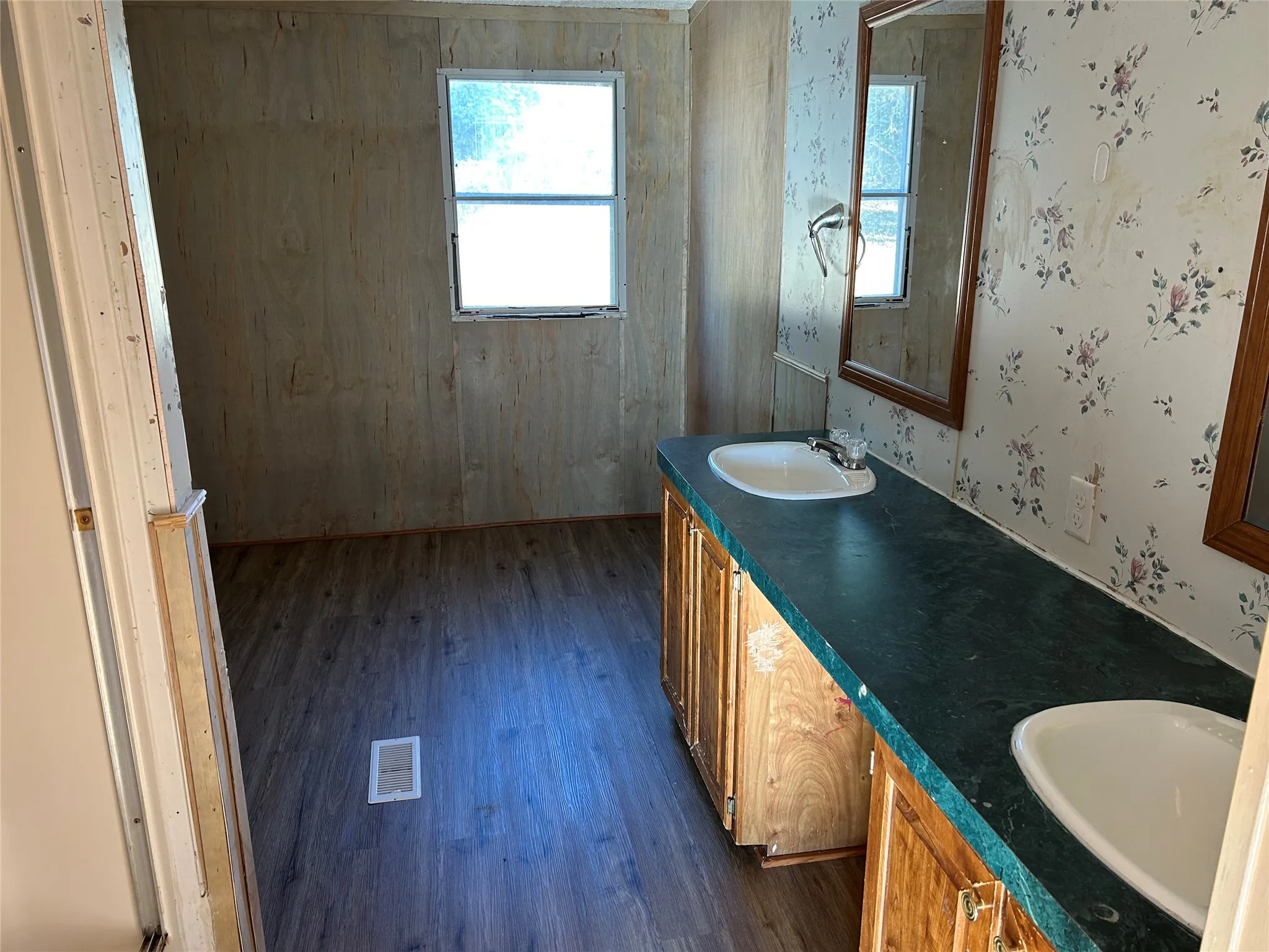 Dual vanity with oval sinks, wood-finish cabinetry, and a dark green countertop