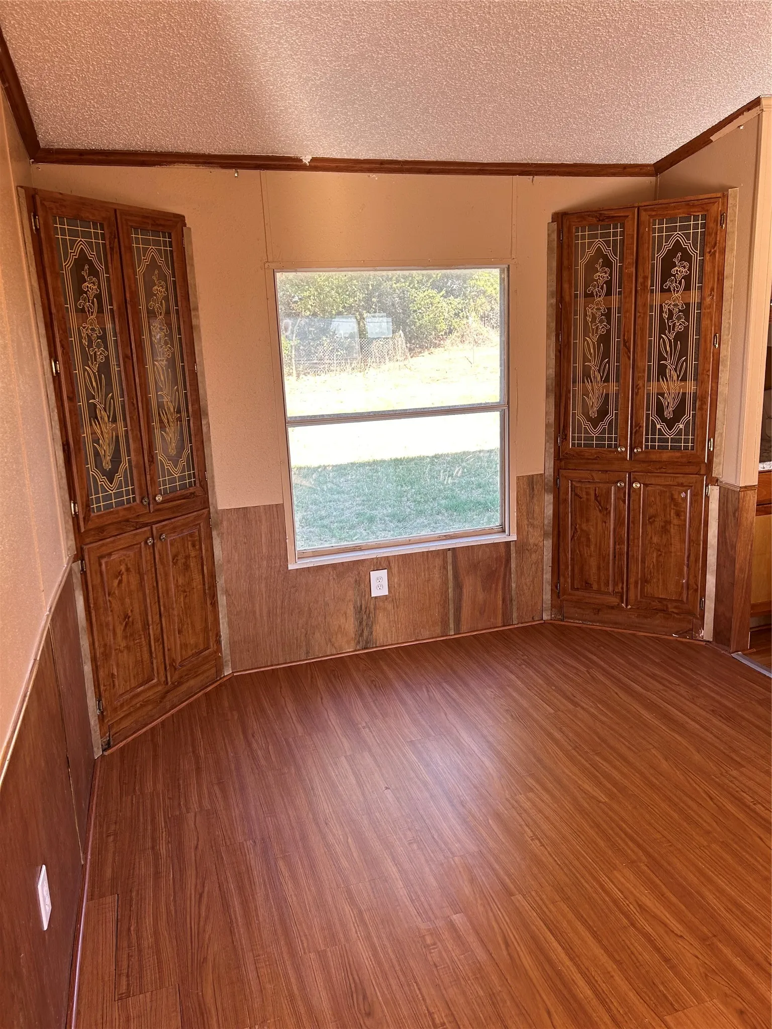 Wood-finish flooring with wood paneling and built-in corner cabinetry featuring decorative glass inserts
