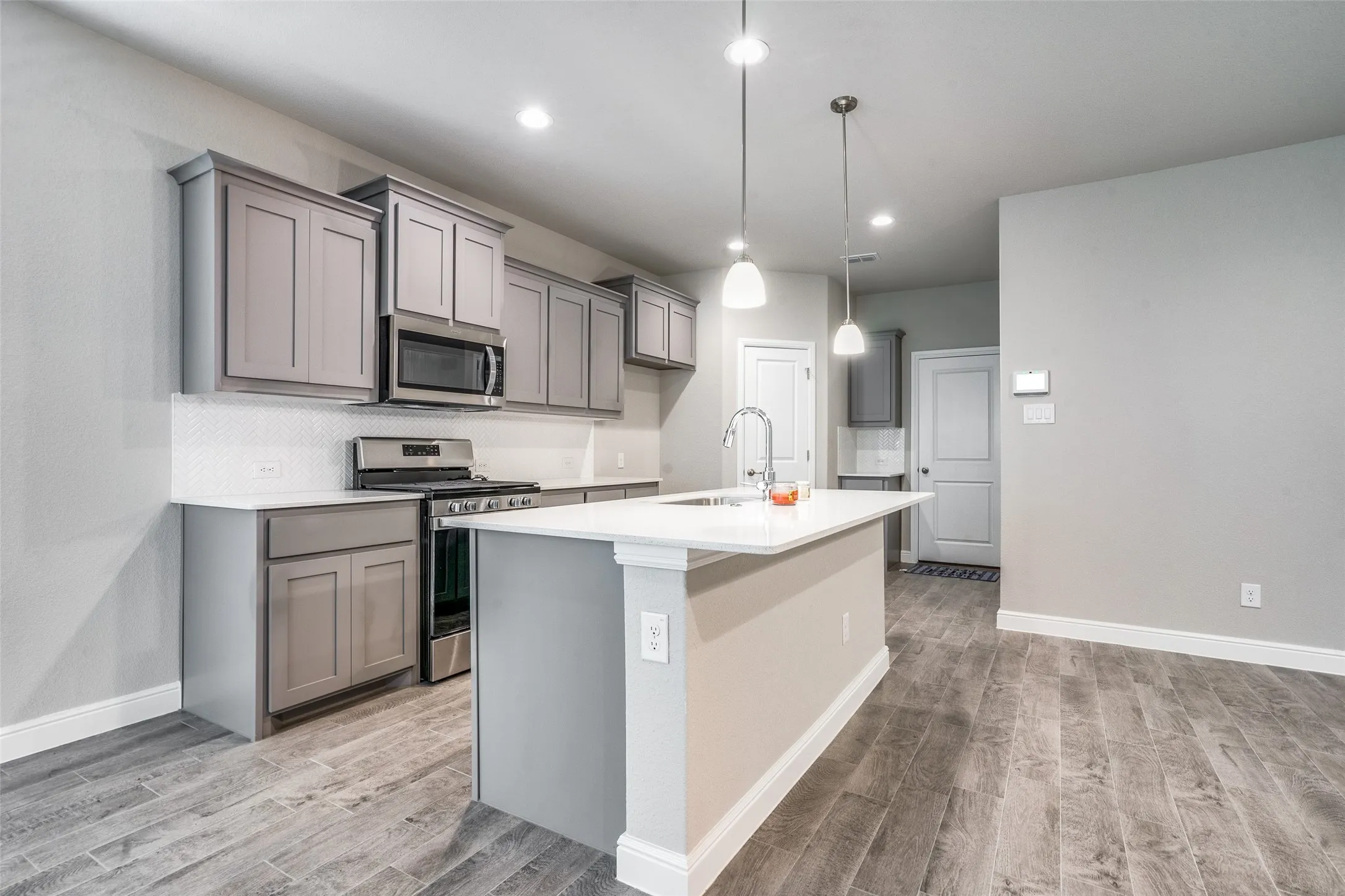 Modern kitchen featuring gray cabinetry with soft-close doors, stainless steel appliances, white quartz countertops, and a large center island with pendant lighting