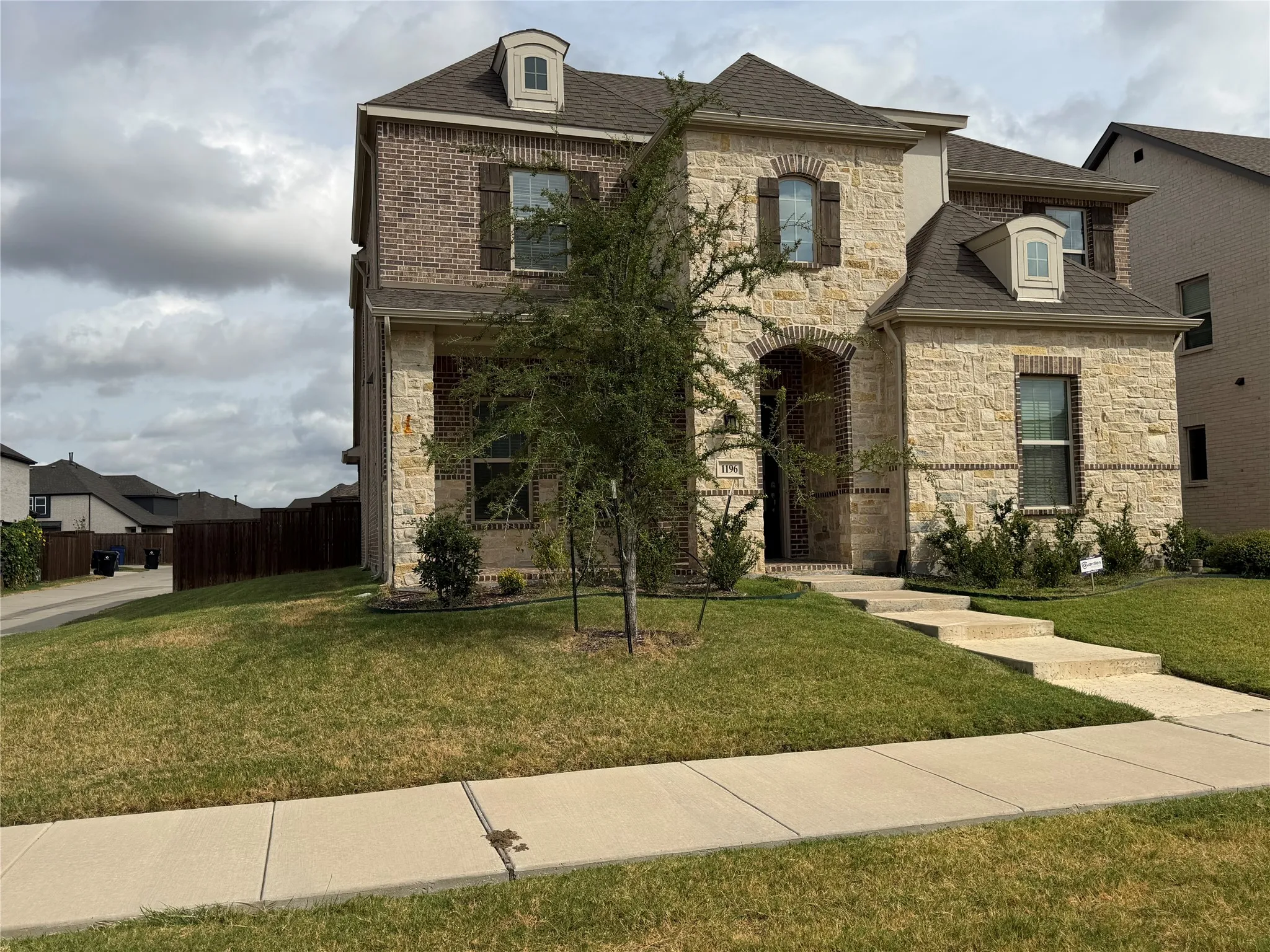 Two-story corner lot with a combination brick and stone facade, dormer windows, and dark wood shutters