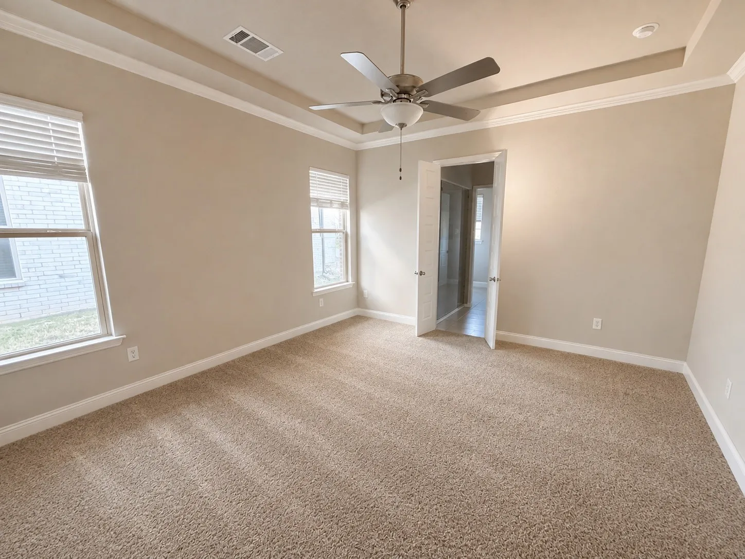 Private primary bedroom in back of the house with recessed ceiling with crown molding, ceiling fan, and light fixture and ensuite bath