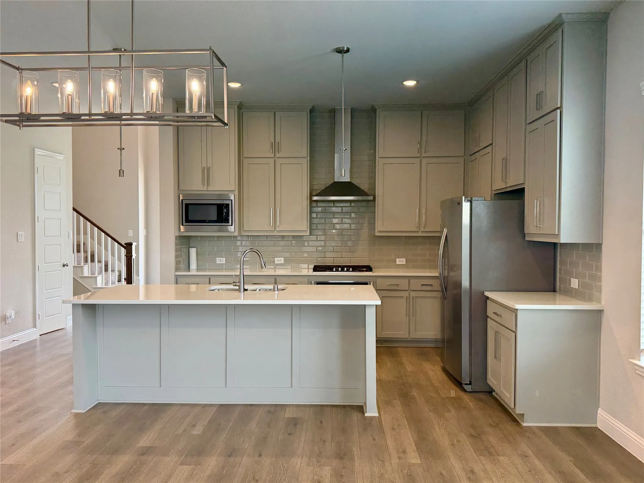 Kitchen featuring a large center island with a sink, light-toned cabinetry, stainless steel appliances, subway tile backsplash, and wood-finish flooring