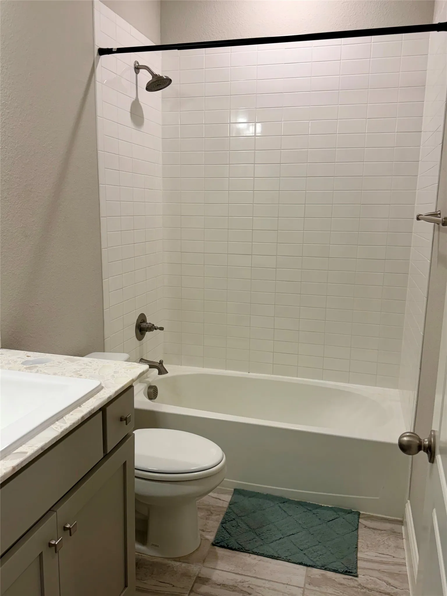 Bathroom featuring a white subway tile shower surround, a white bathtub, and a single vanity with a light-colored countertop