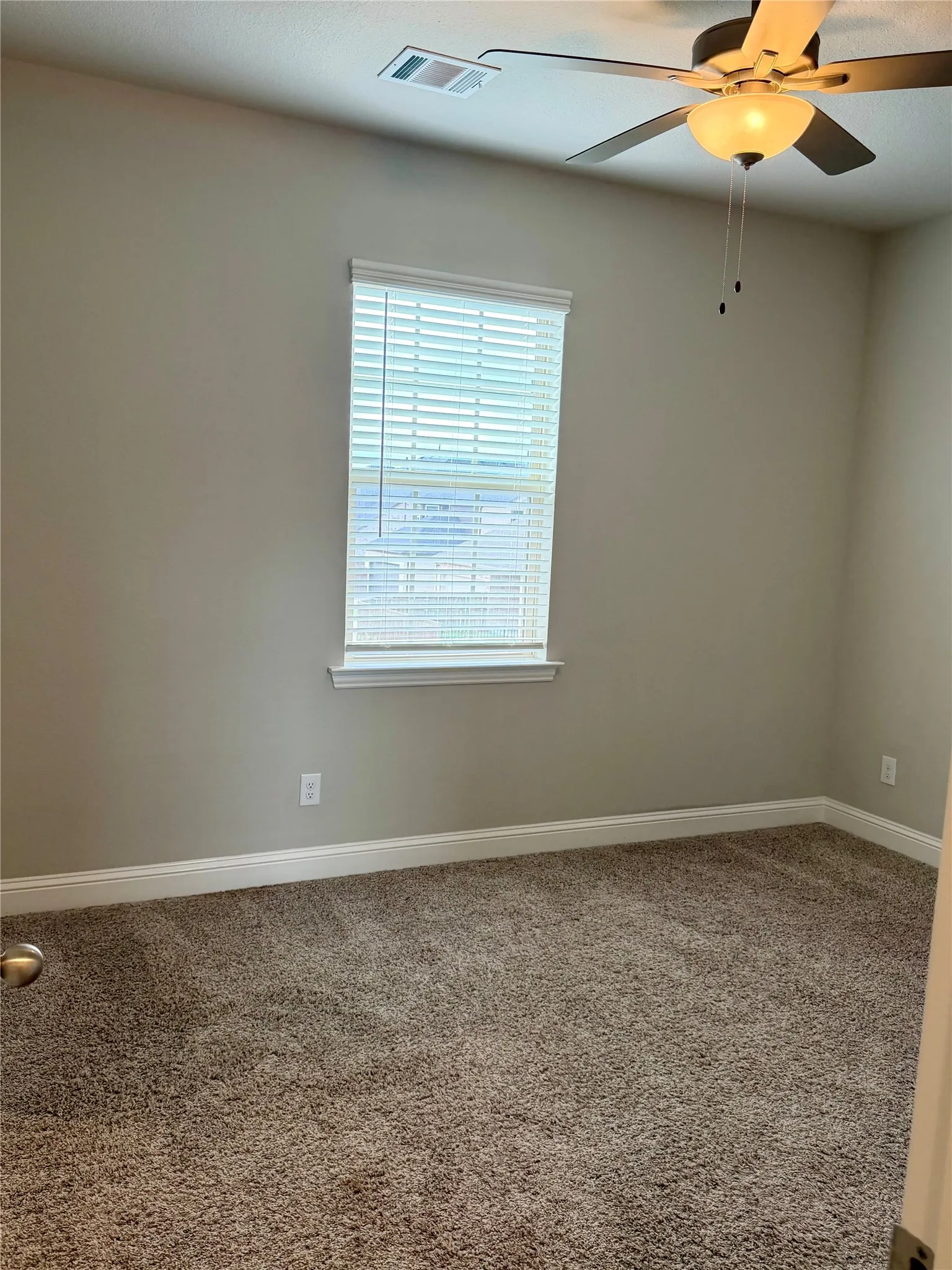 Plush carpeting, neutral wall tones, window with horizontal blinds, and a ceiling fan with integrated lighting