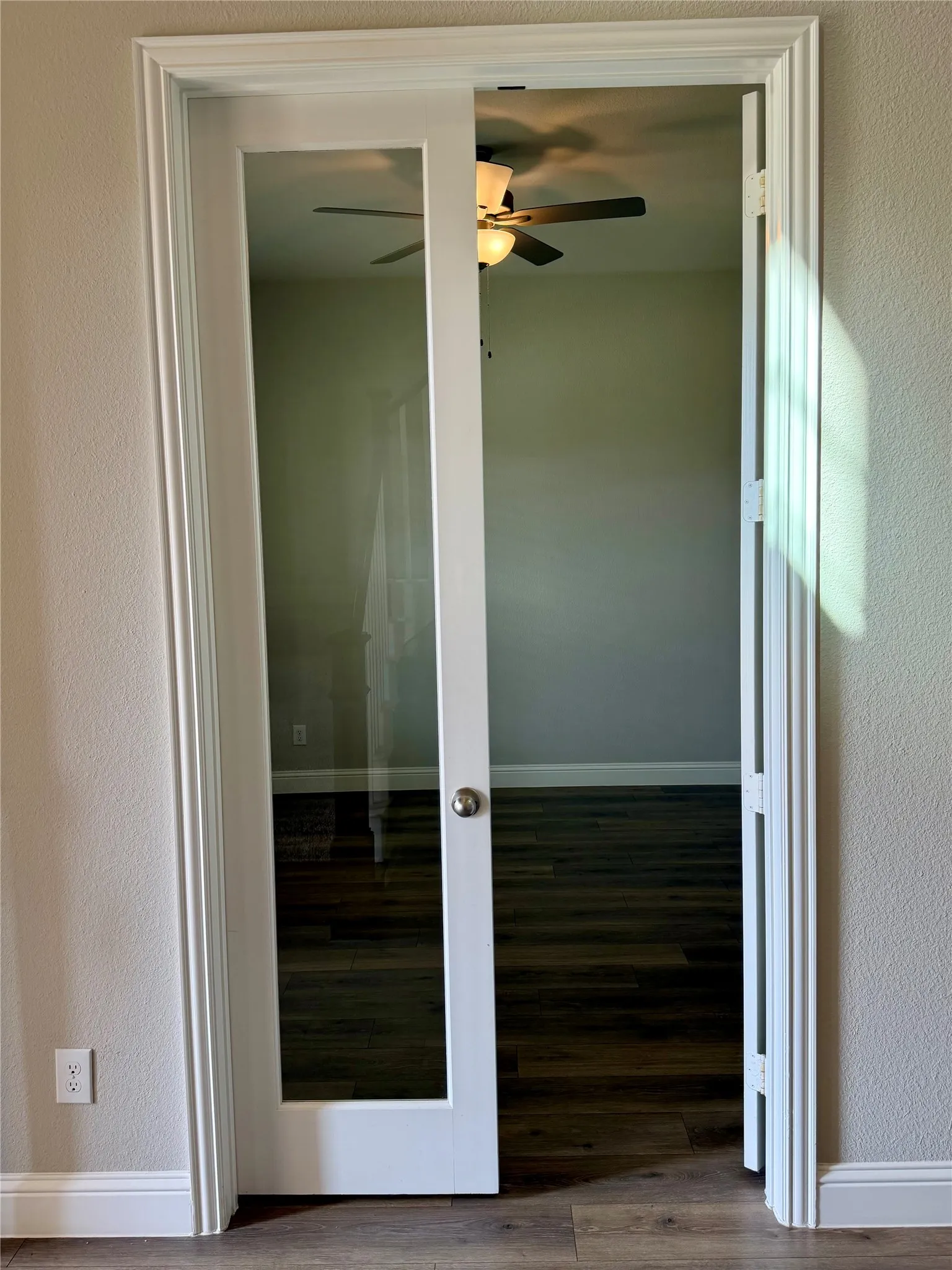 Study with double French doors with clear glass panels, wood-finish flooring, and a ceiling fan with integrated lighting to the left of entry