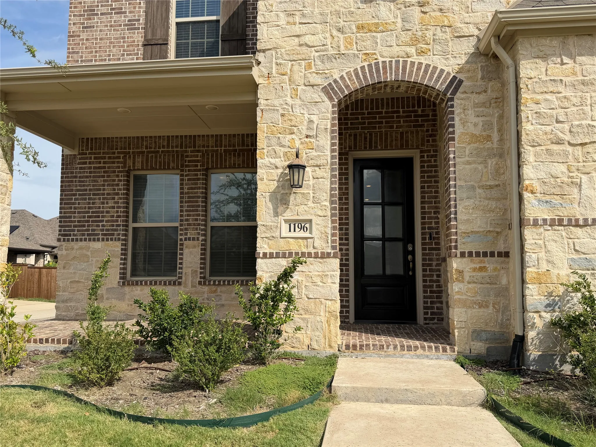 Brick and stone exterior with covered front porch, arched brick doorway, and a black paneled door
