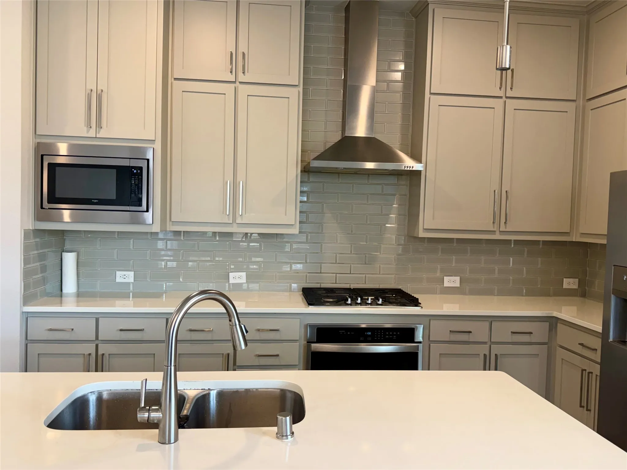 Kitchen featuring light gray cabinetry, white countertops, glass subway tile backsplash, stainless steel appliances, and a kitchen island with an undermount sink