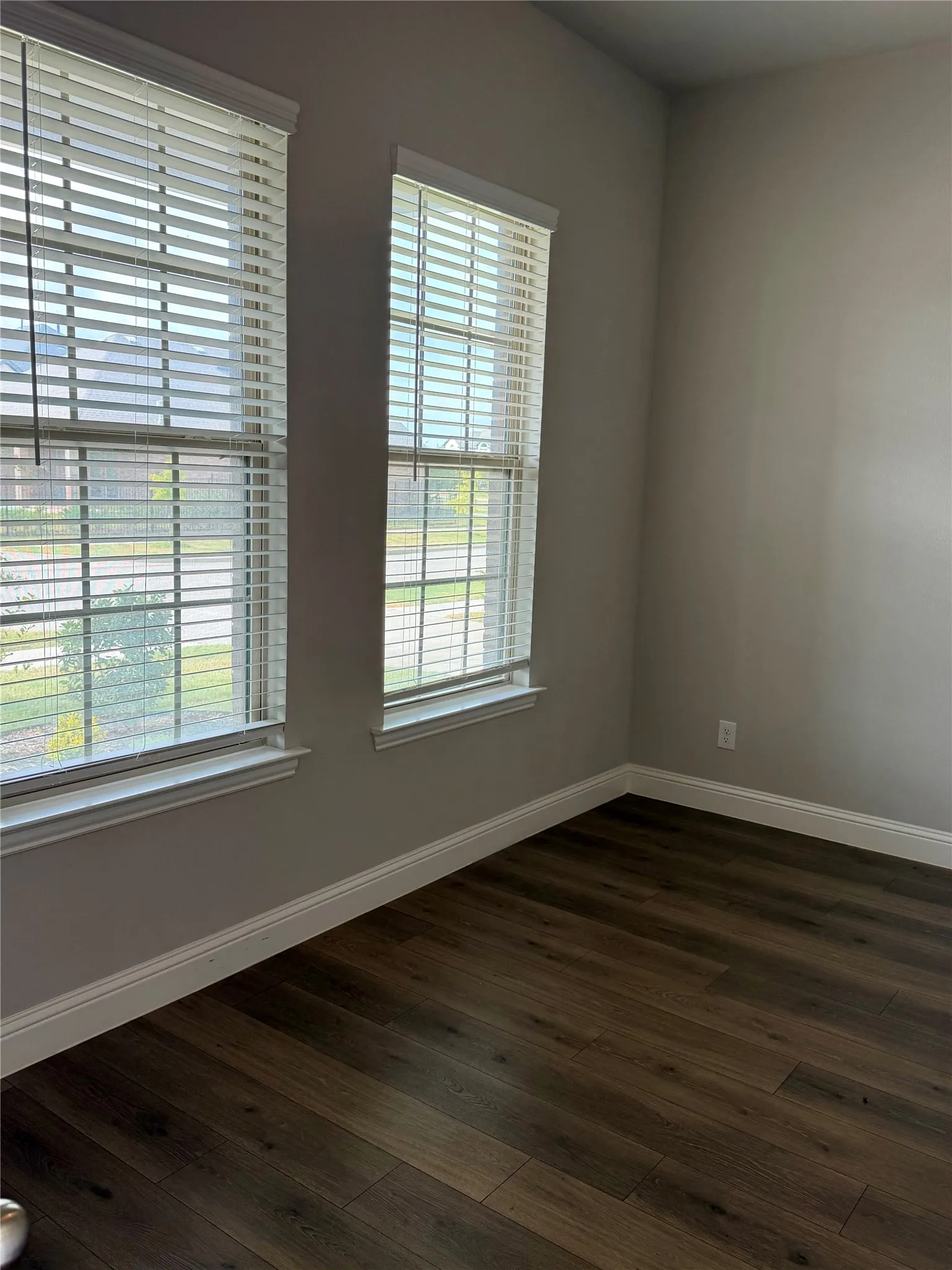 Wood-finish flooring with white baseboards, two windows featuring white blinds, and neutral-toned walls