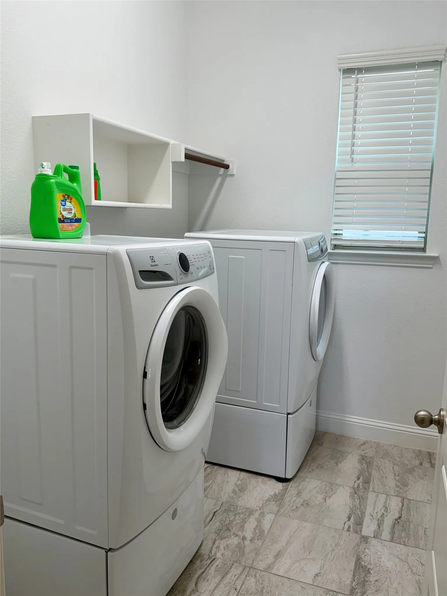 Laundry area equipped with washer and dryer featuring tile flooring, white walls, built-in shelving, a clothes rod, and a window with blinds