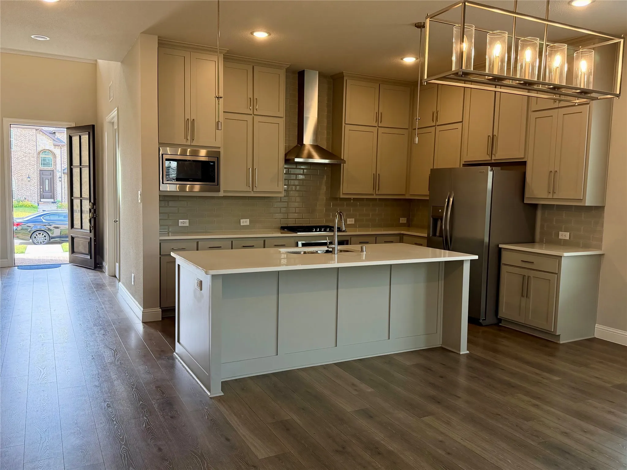 Modern kitchen featuring wood-finish flooring, a large central island with a light-colored countertop, abundant cabinetry, and stainless steel appliances
