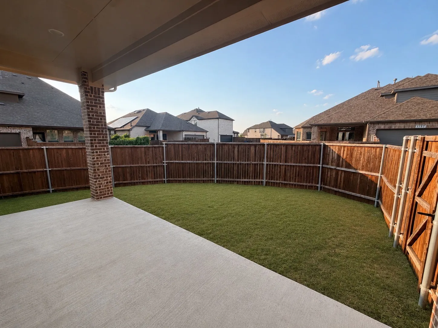 Covered patio with a brick column, concrete flooring, and an expansive lawn area