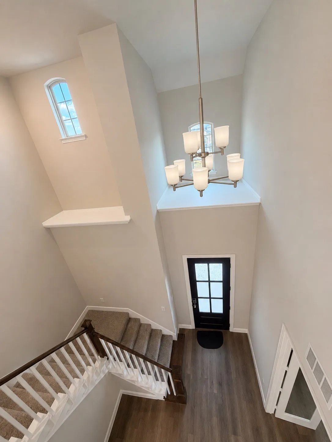 View of entry from upstairs of the two-story entry featuring high ceilings, wood-finish flooring, a contemporary chandelier, and a black paneled door with divided lites