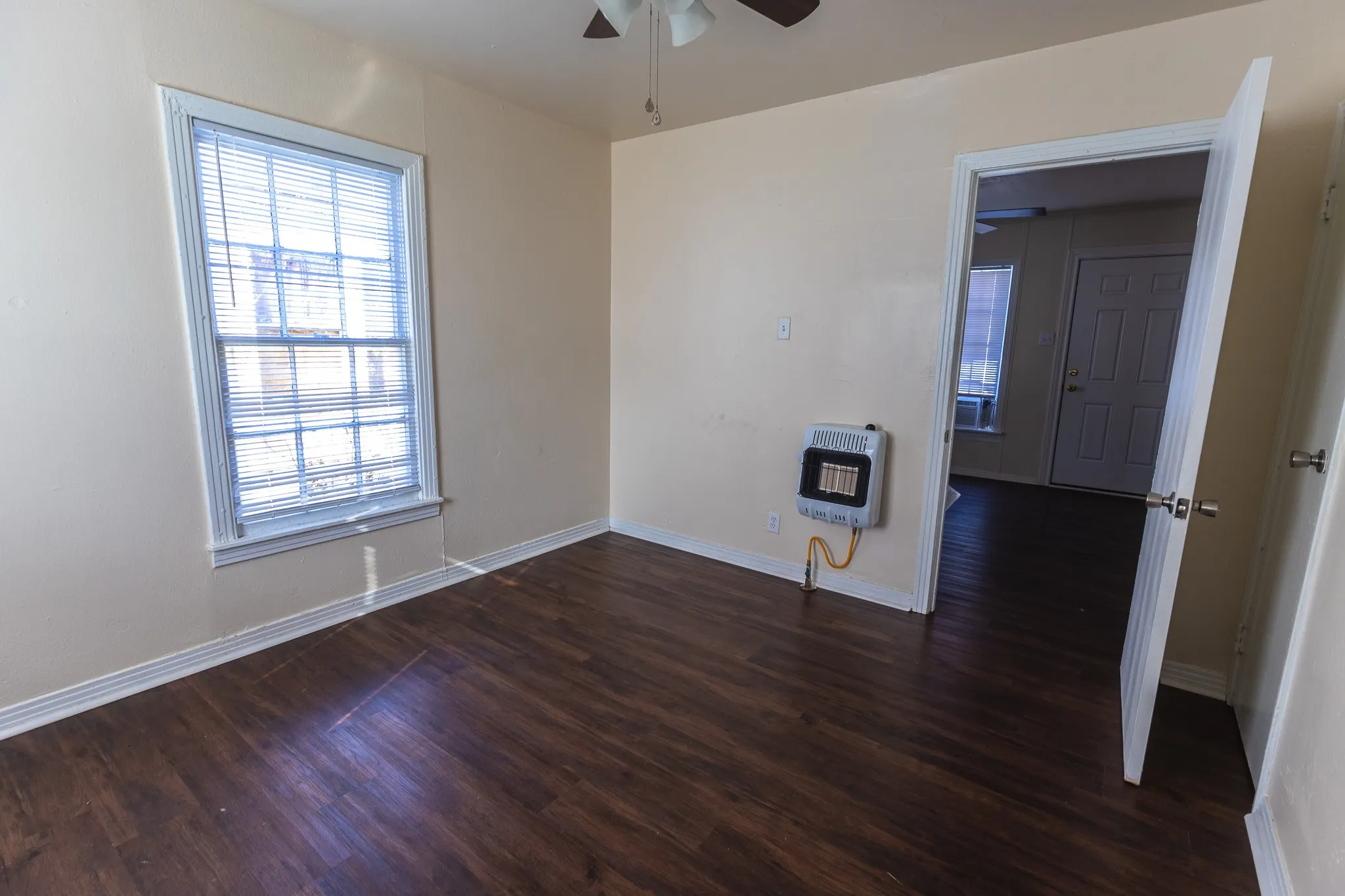 Bright corner bedroom featuring hardwood flooring, large double-hung window with plantation shutters, and neutral wall finishes