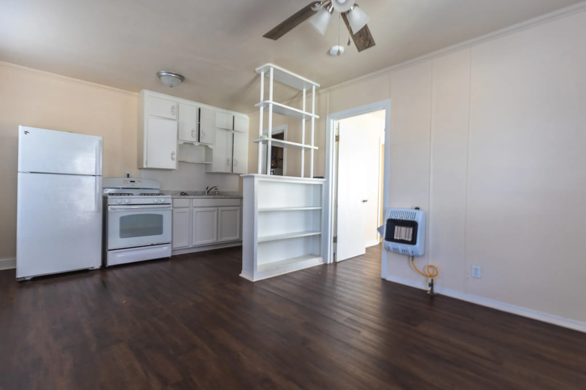 Open-concept kitchen and living area featuring stainless steel appliances, white cabinetry with upper glass-front storage, wood-finish flooring throughout, and abundant natural light from multiple windows