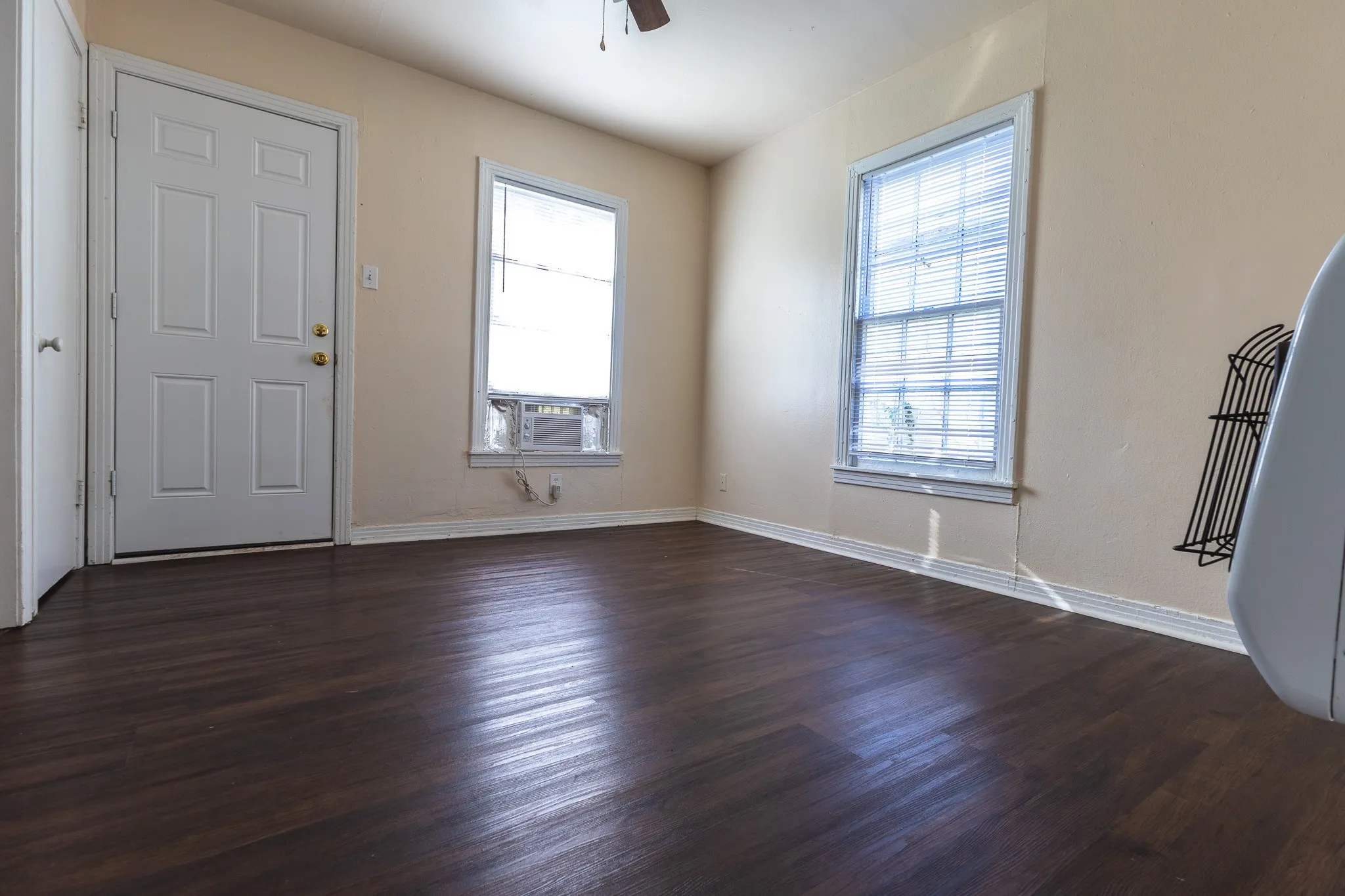 Wood-finish flooring, neutral wall tones, multiple windows with blinds, and an integrated window air conditioning unit