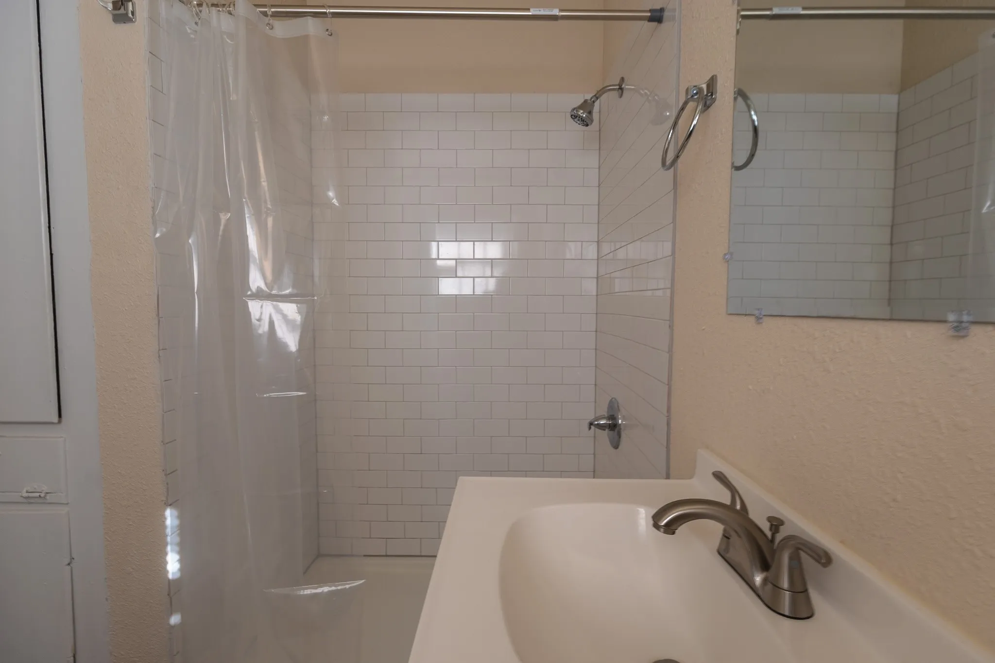 Bathroom featuring a shower with white subway tile surround, brushed nickel fixtures, a vanity with an integrated sink, and a wall-mounted mirror