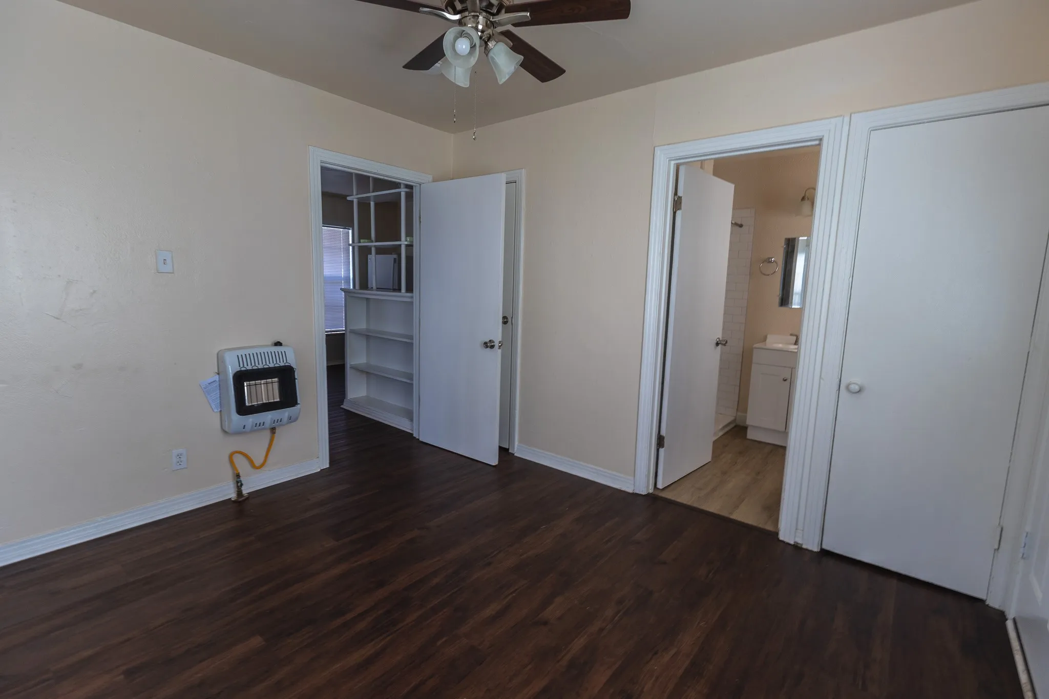 Wood-finish flooring, ceiling fan with integrated lighting, built-in shelving, white paneled doors, and a wall-mounted heater