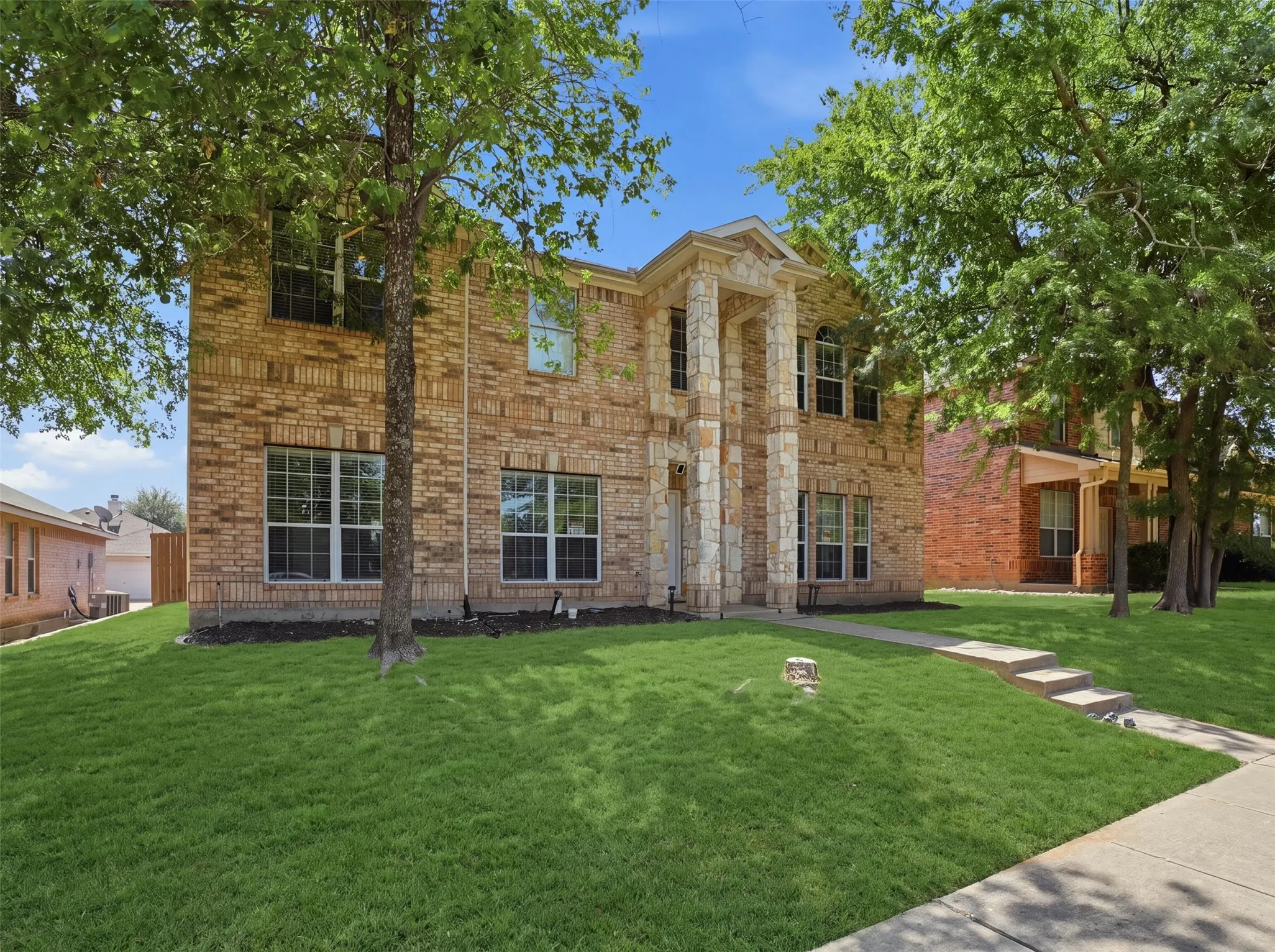 Two-story brick exterior with stone accents, featuring a prominent columned entryway and multiple large windows