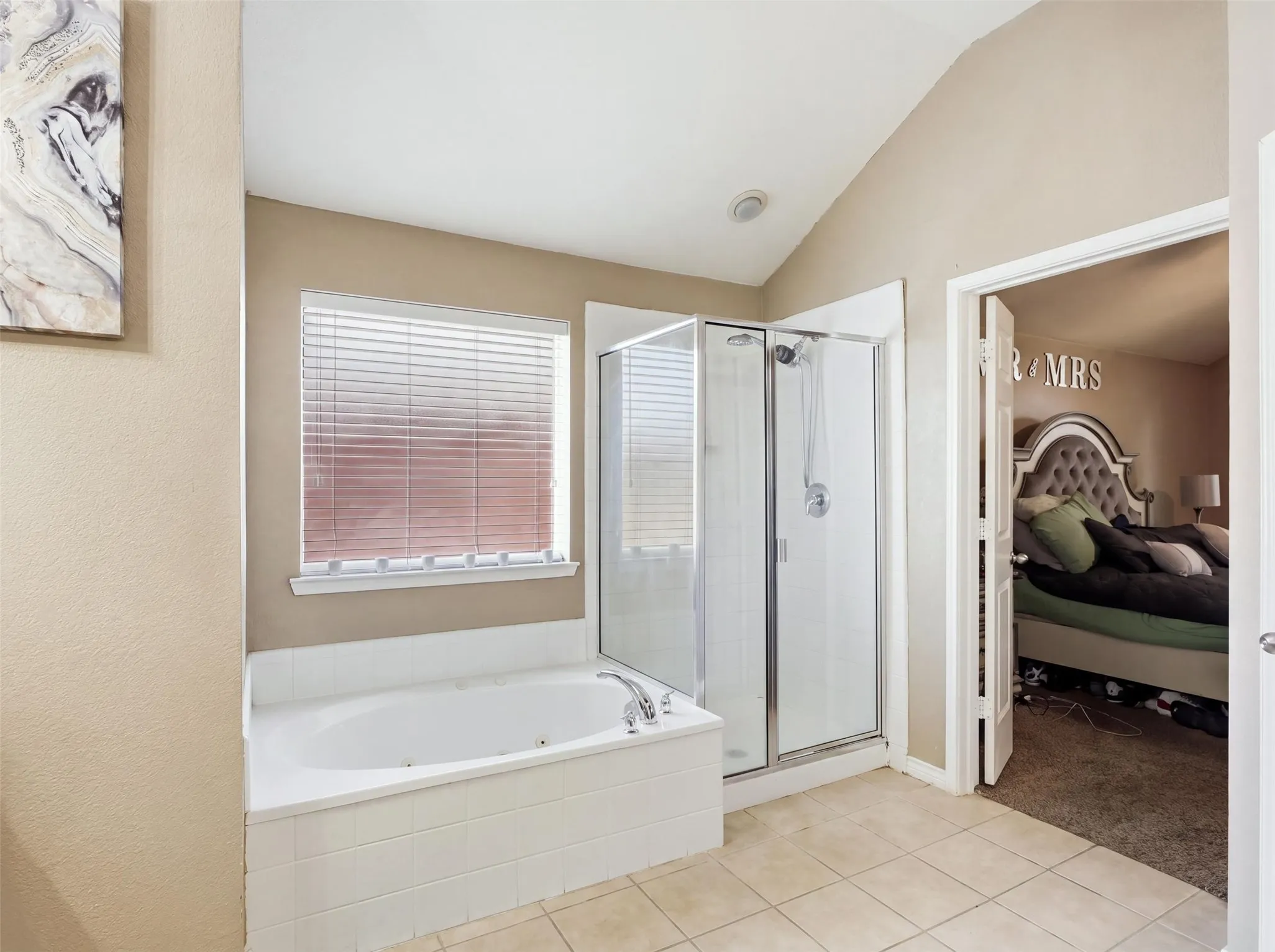 Soaking tub with tiled surround, adjacent glass-enclosed shower, tile flooring, and vaulted ceiling